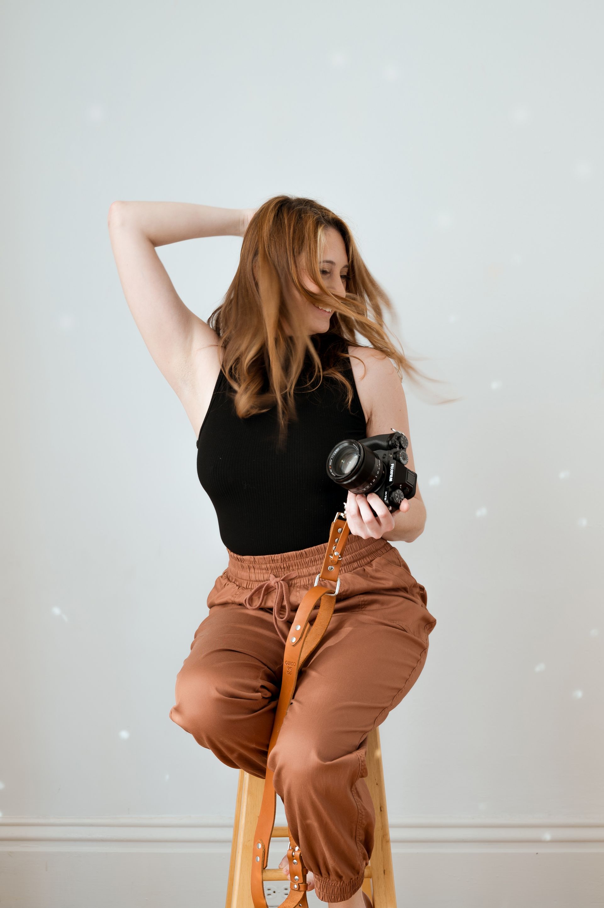 A woman is sitting on a stool holding a camera.