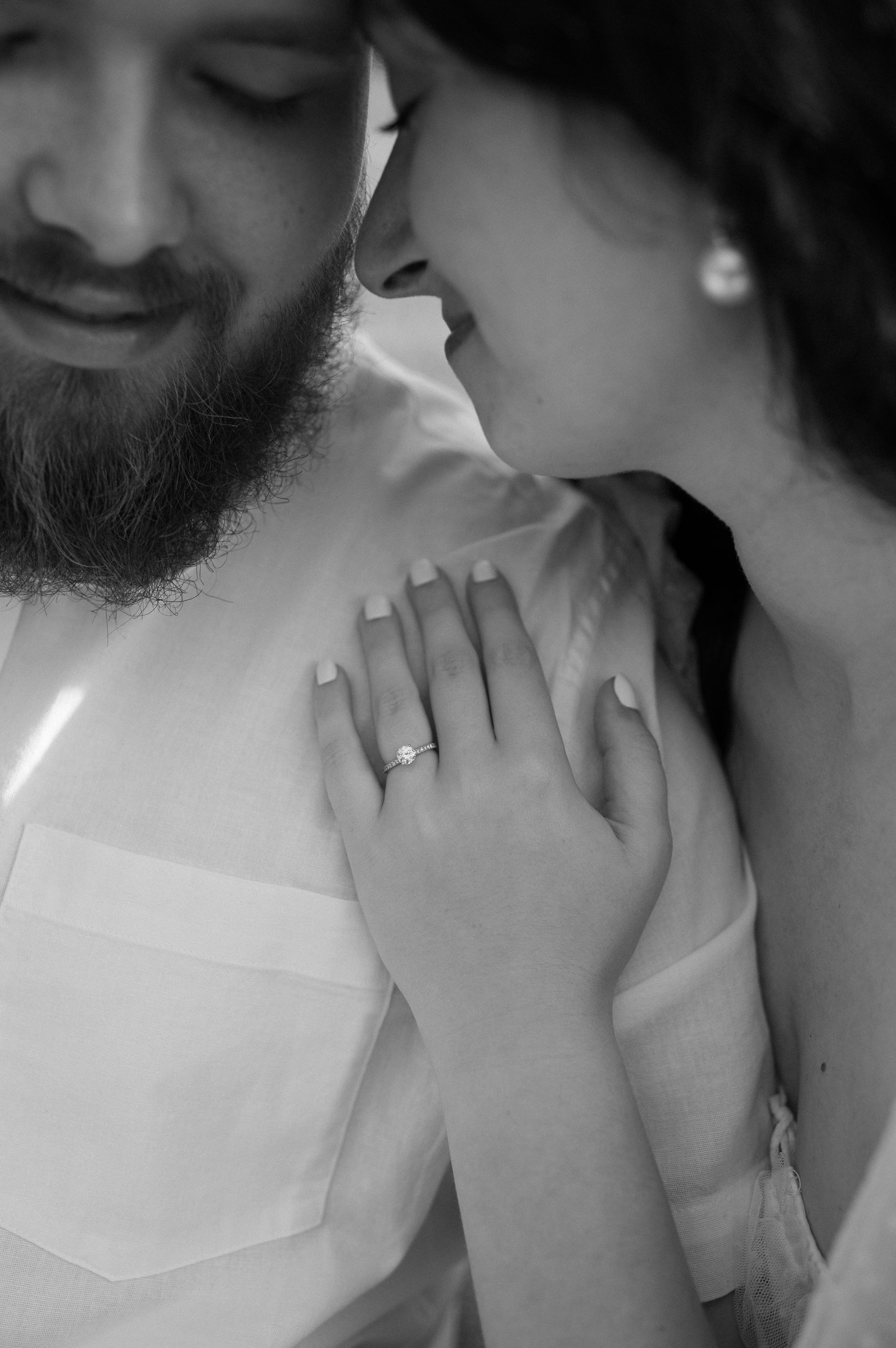 A black and white photo of a bride and groom kissing . the bride is wearing a wedding ring.