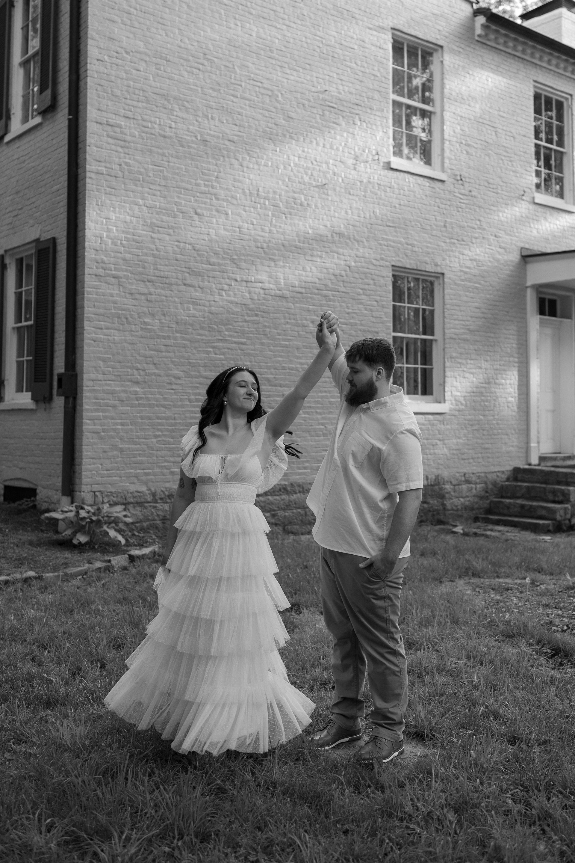 A black and white photo of a bride and groom dancing in front of a brick building.