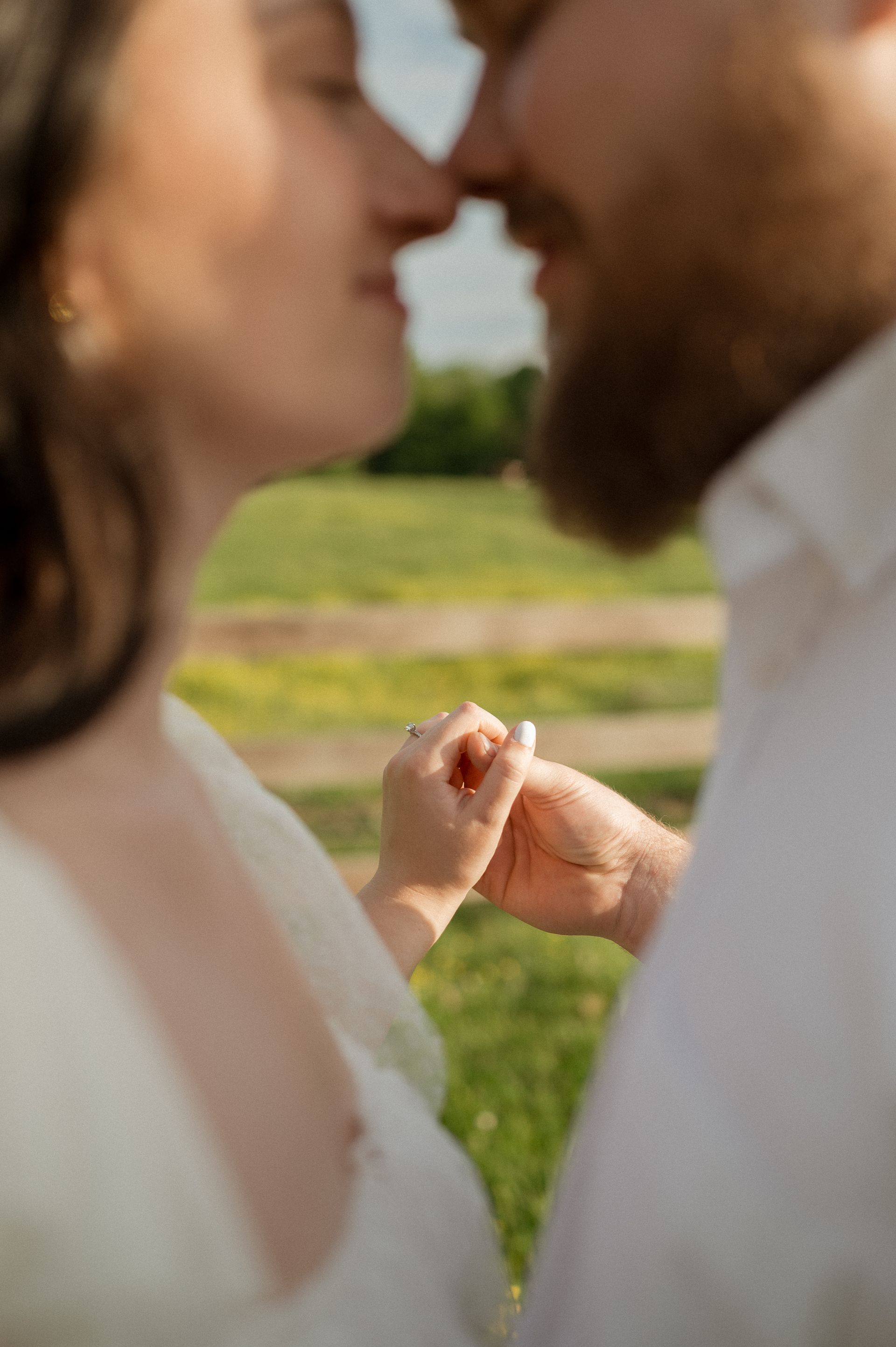 A man and a woman are kissing in a field and the woman is holding the man 's hand.