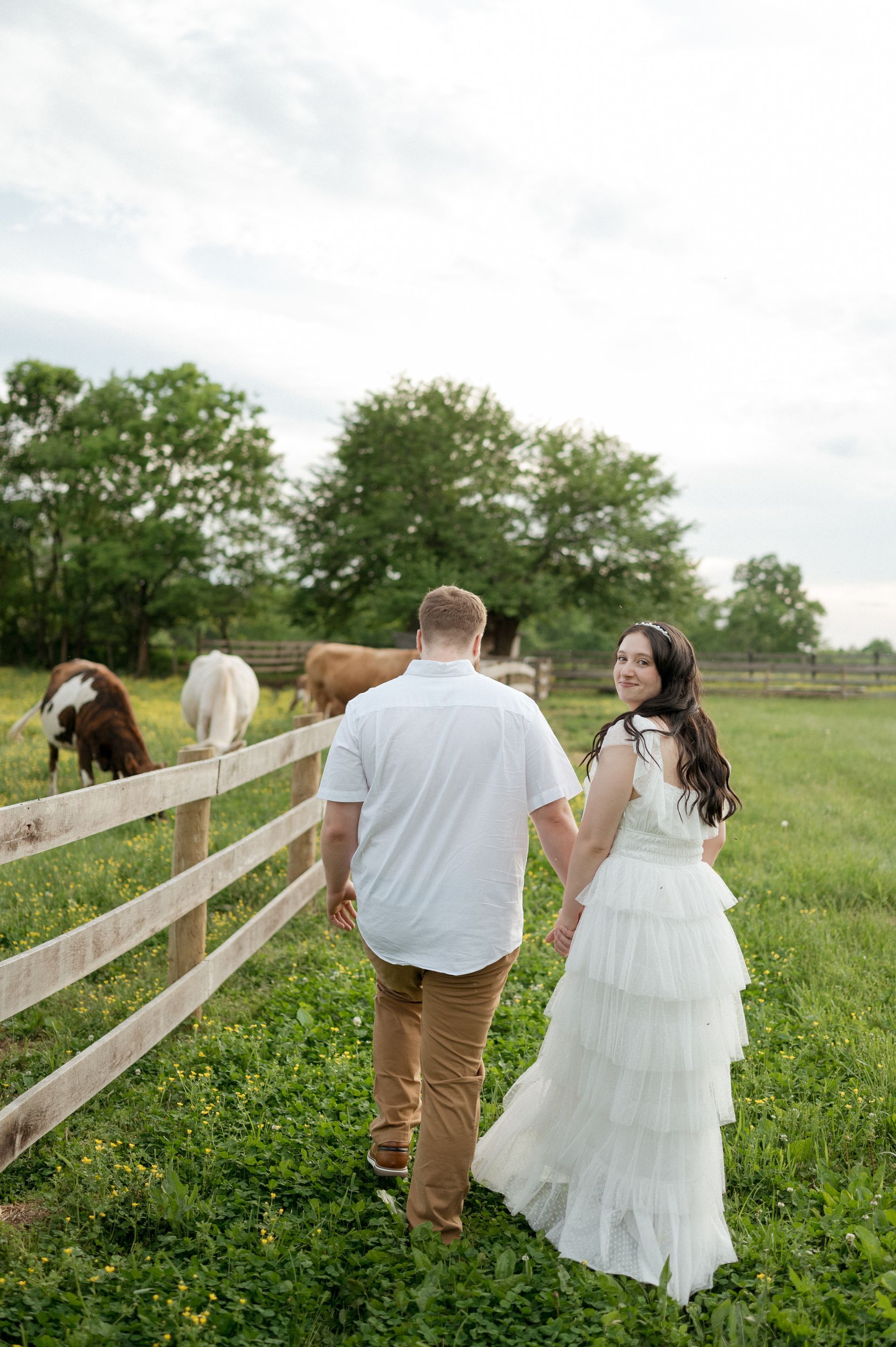A man and a woman are walking in a field with horses behind a fence.