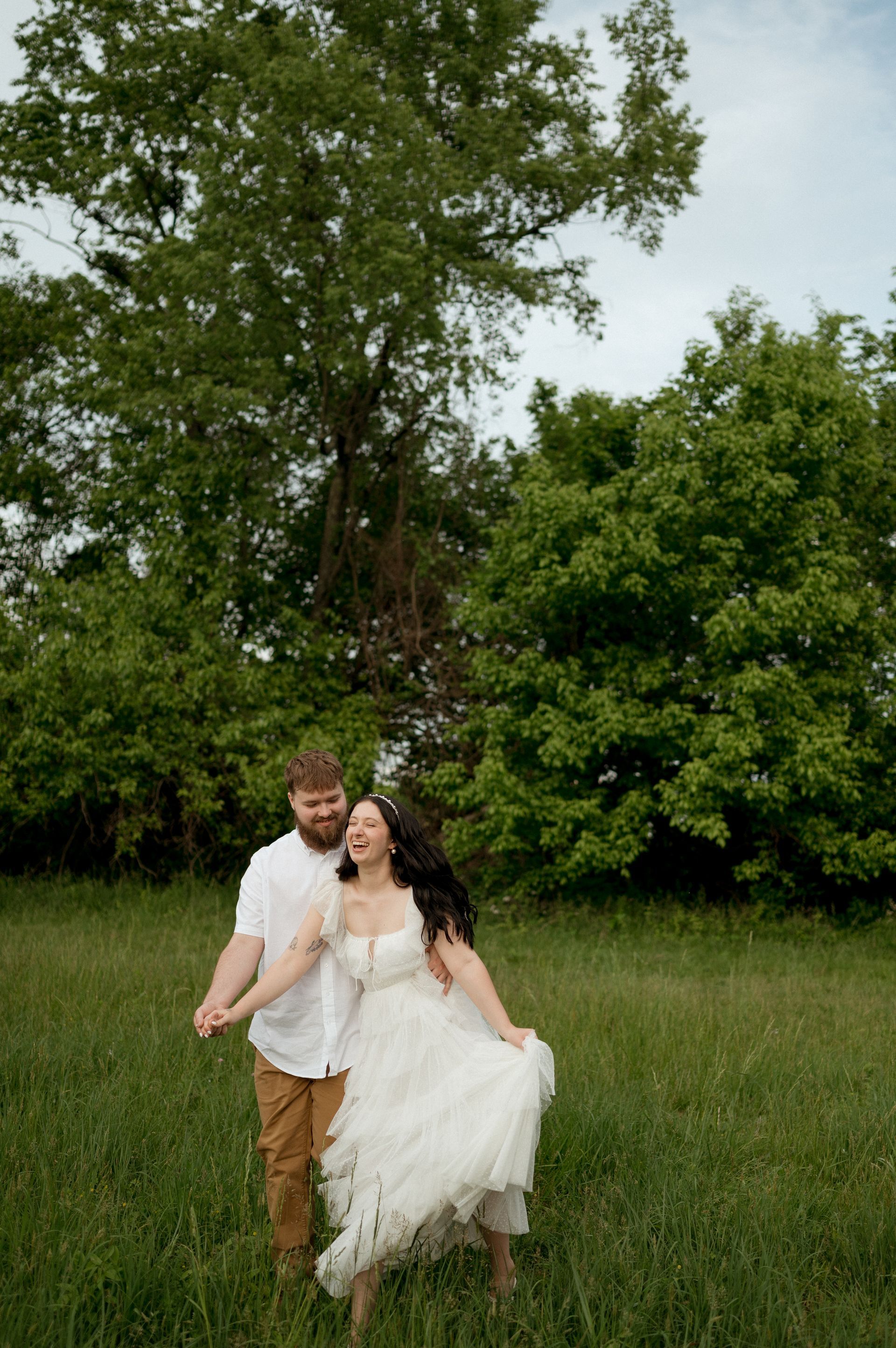 A man and a woman are holding hands in a field . the woman is wearing a white dress.