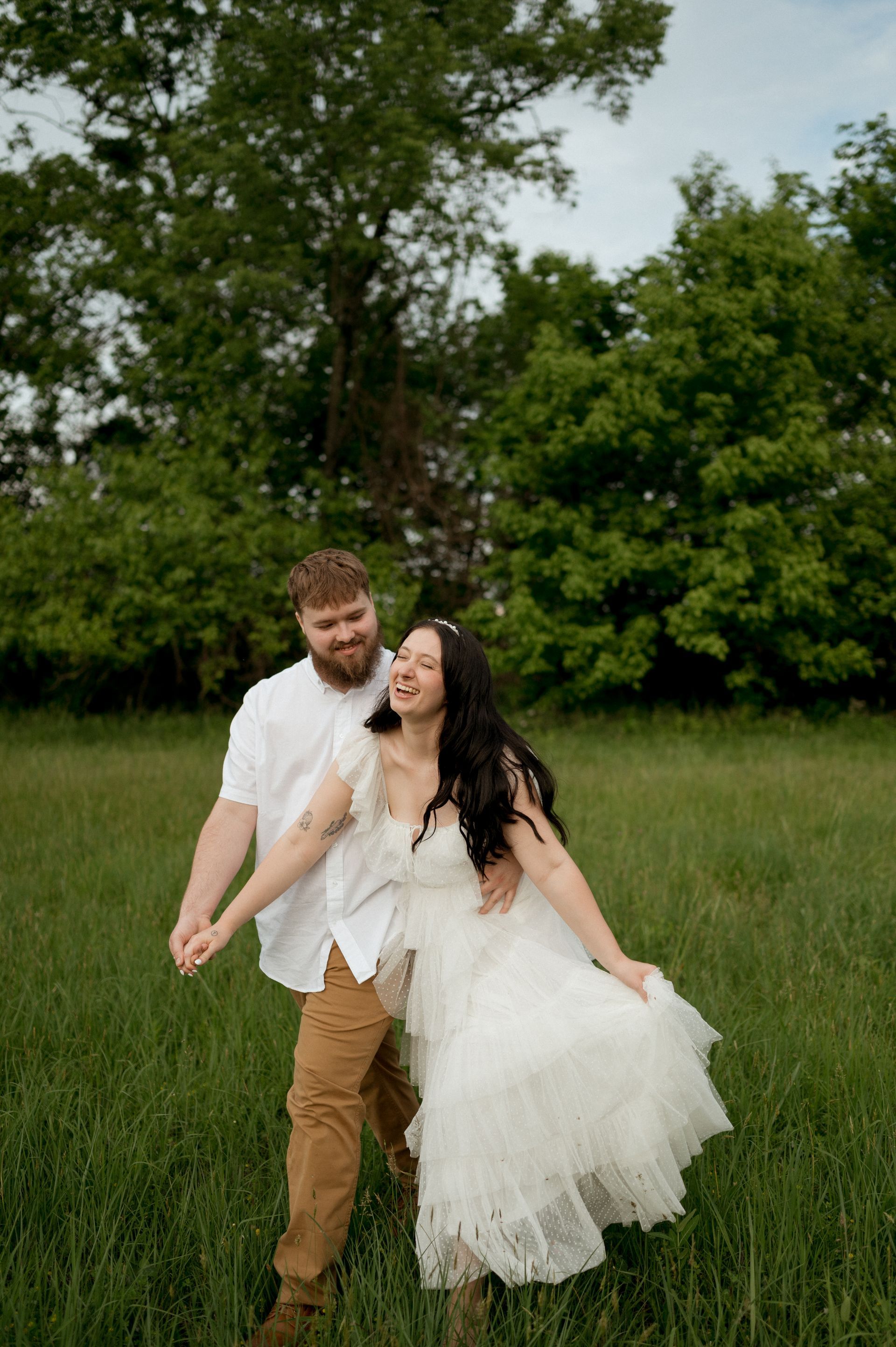 A man and a woman are holding hands in a field . the woman is wearing a white dress.