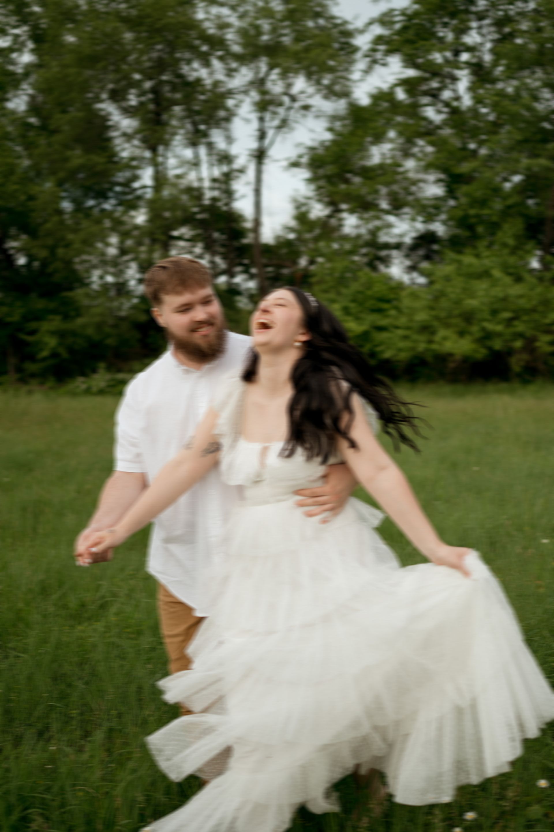 A man is holding a woman in a white dress in a field.
