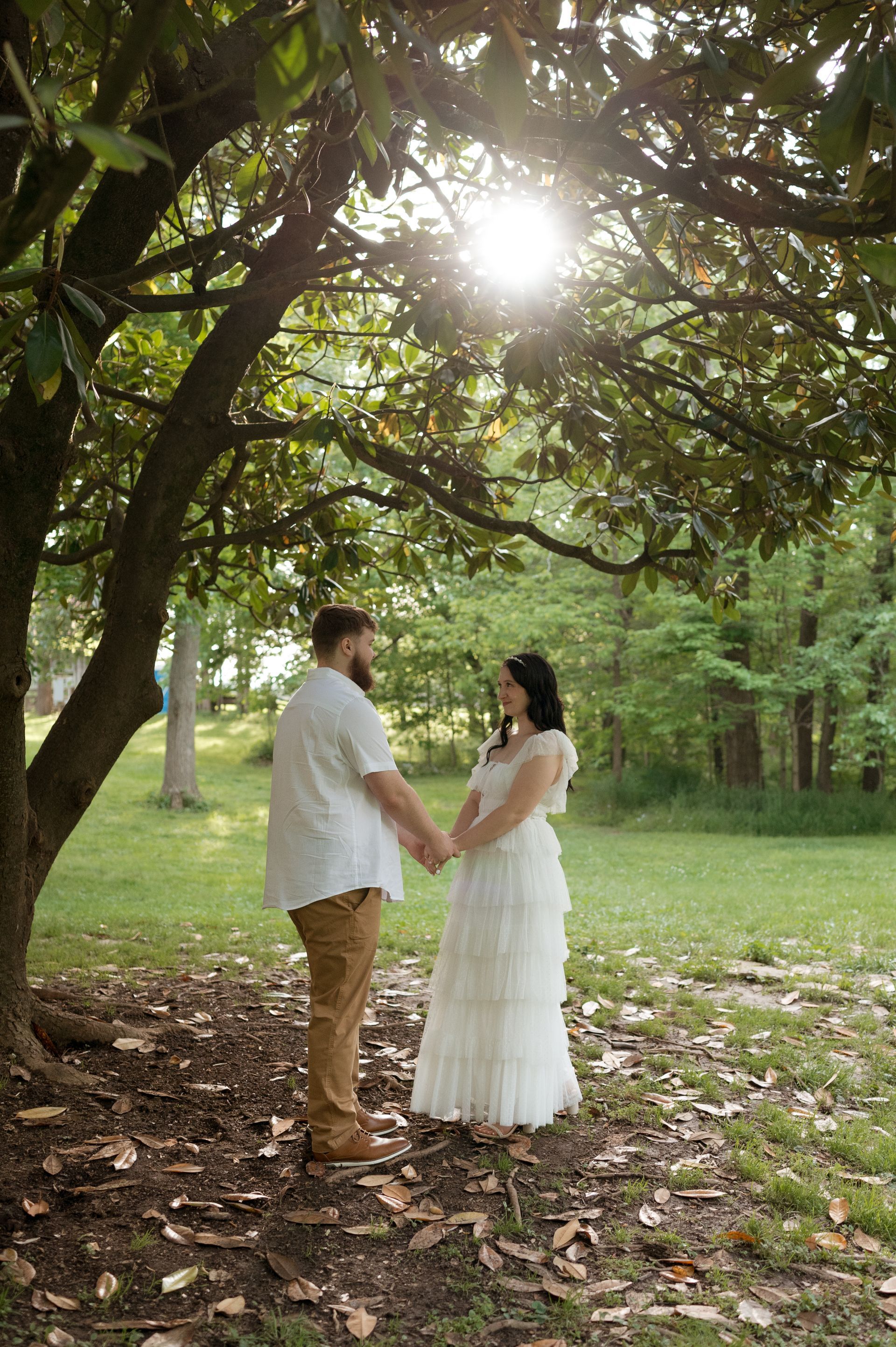 A man and a woman are standing under a tree holding hands.