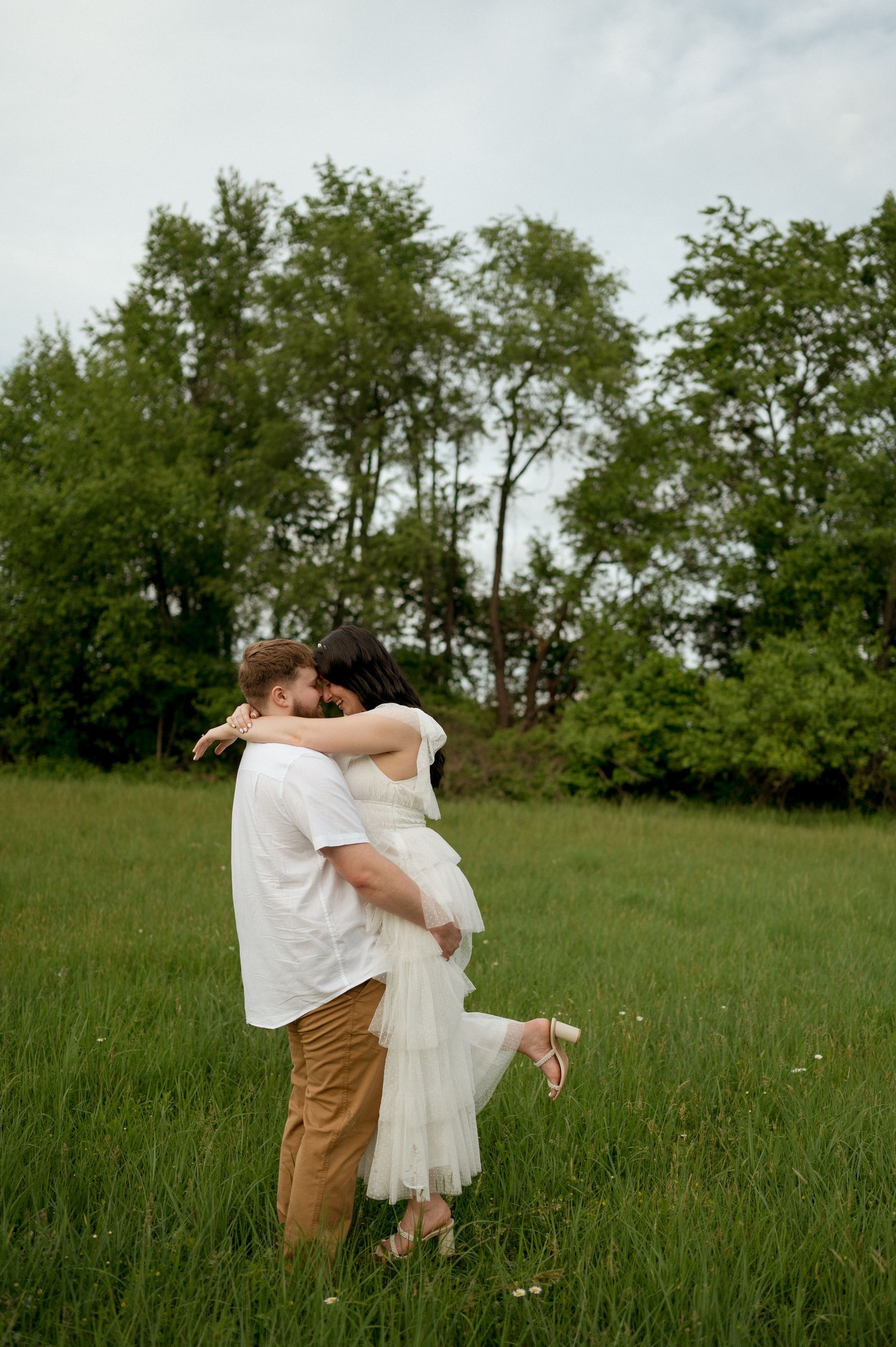 A man is holding a woman in his arms in a field.