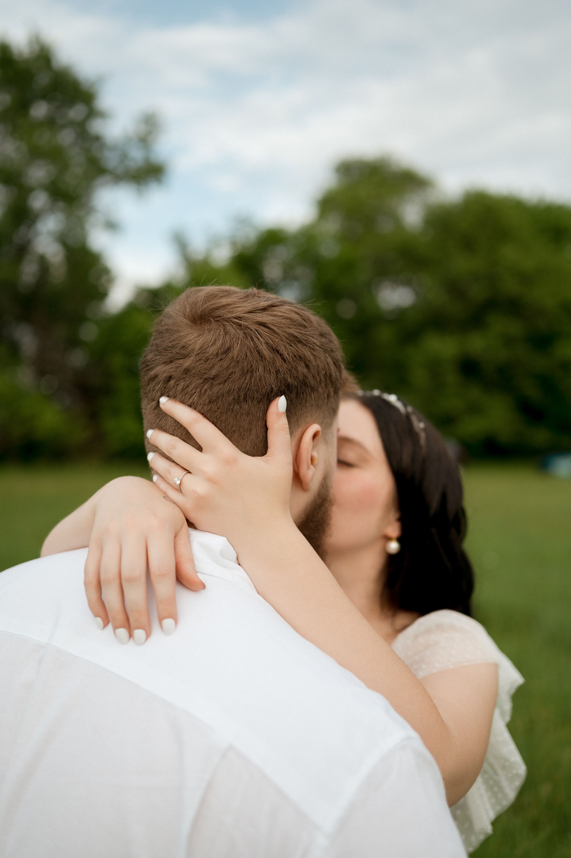 A bride and groom kissing in a field with trees in the background