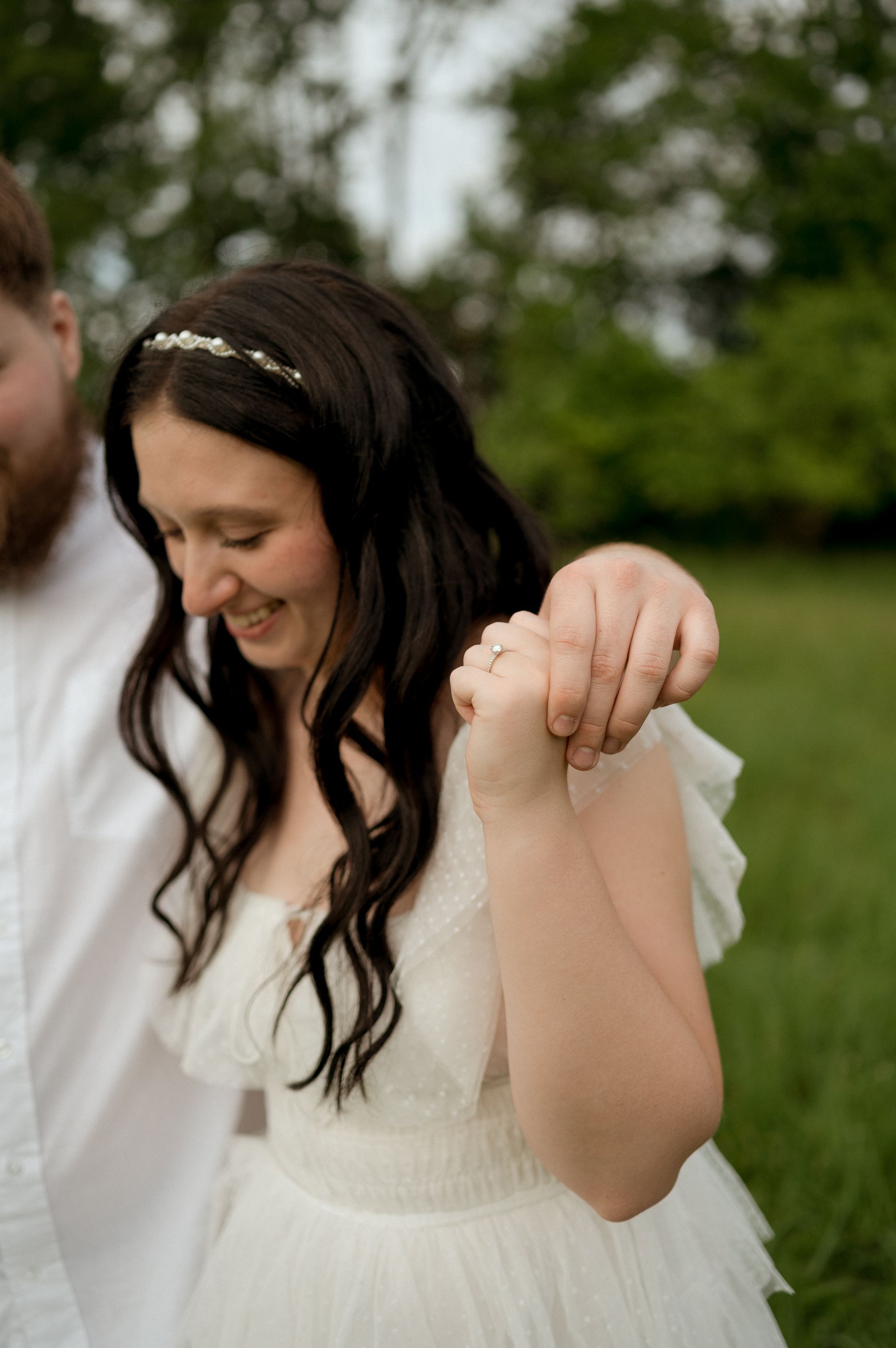 A woman in a white dress is holding a man 's hand in a field.