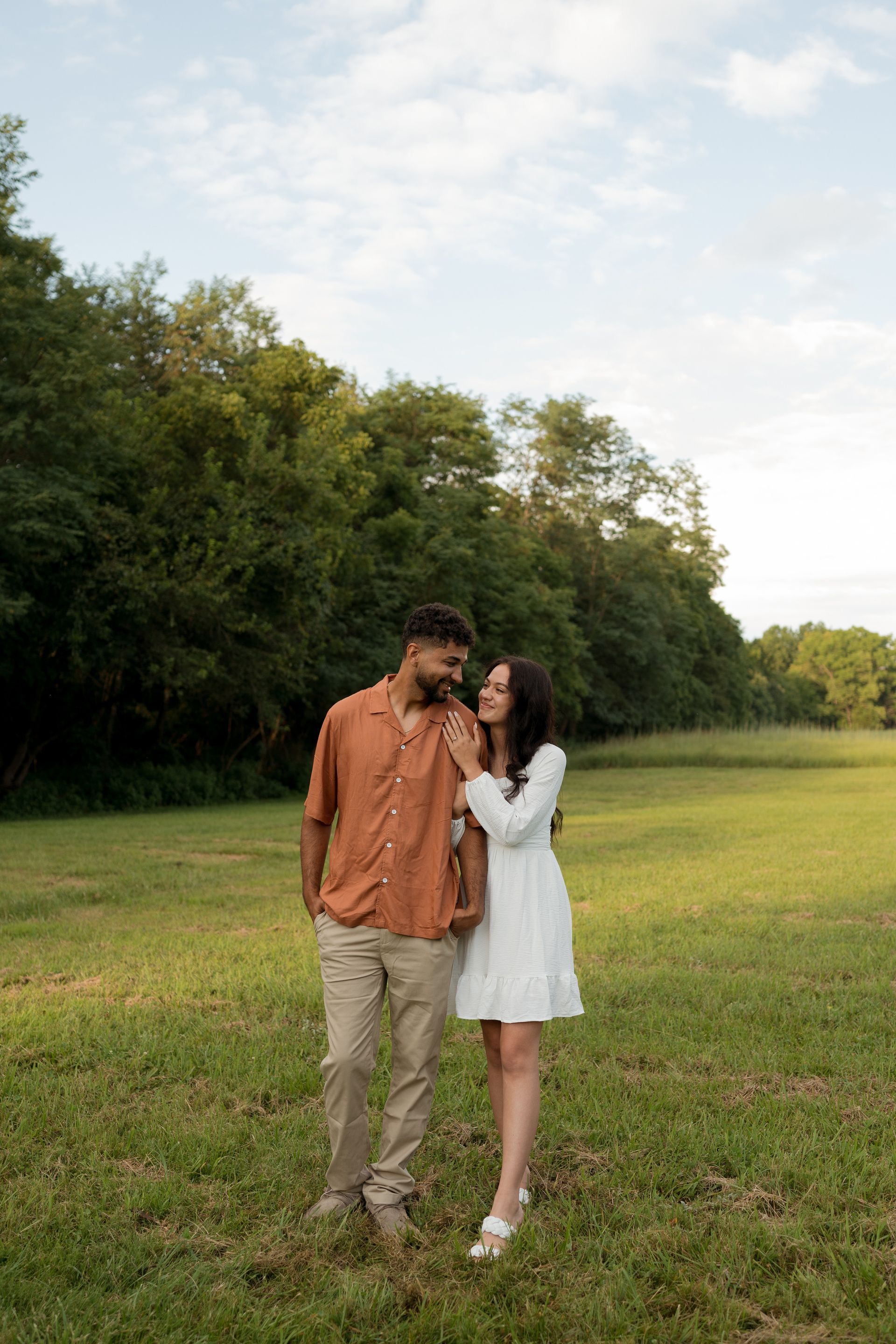 A man and a woman are standing in a field holding hands.