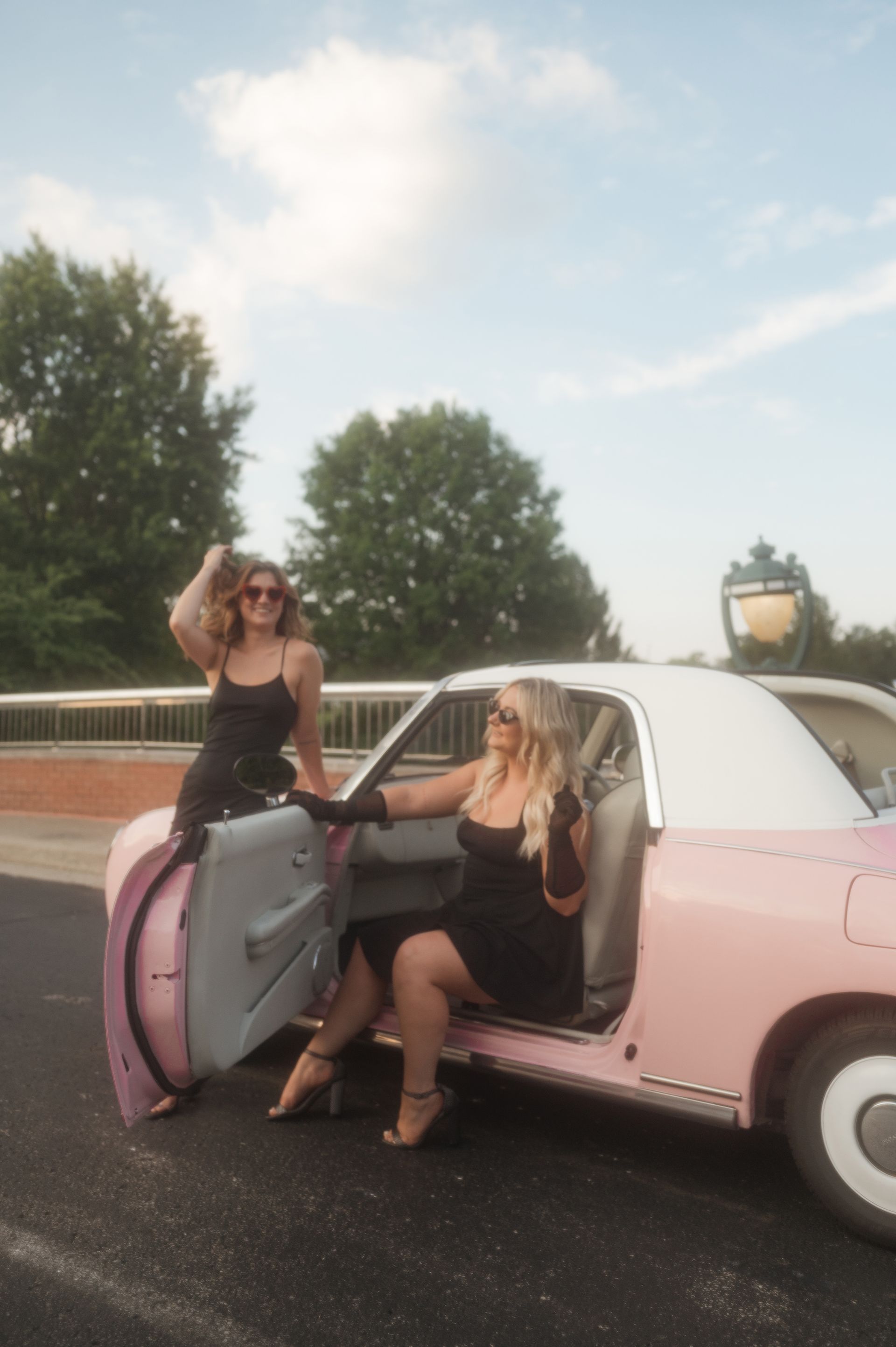 Two women in black dresses are sitting in a pink car