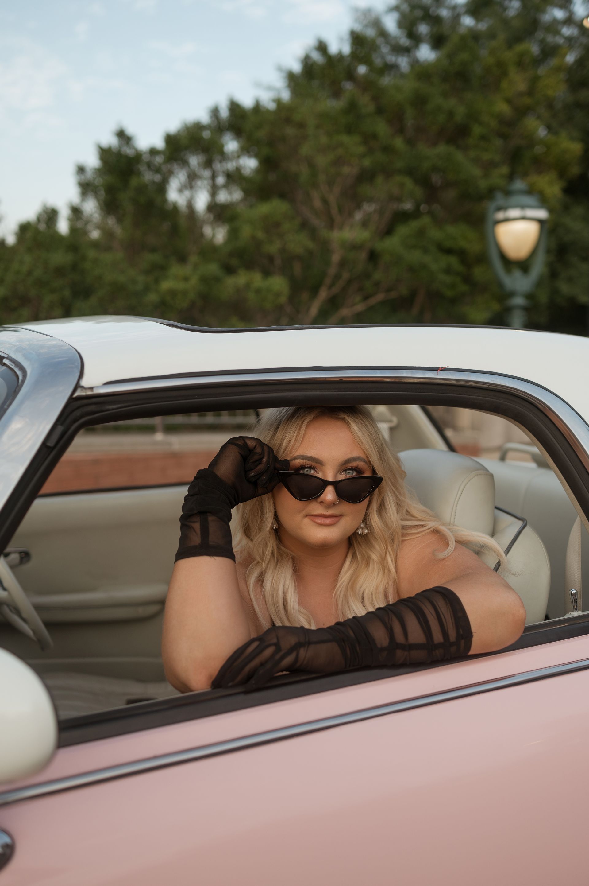 A woman wearing sunglasses and gloves is sitting in a pink car.