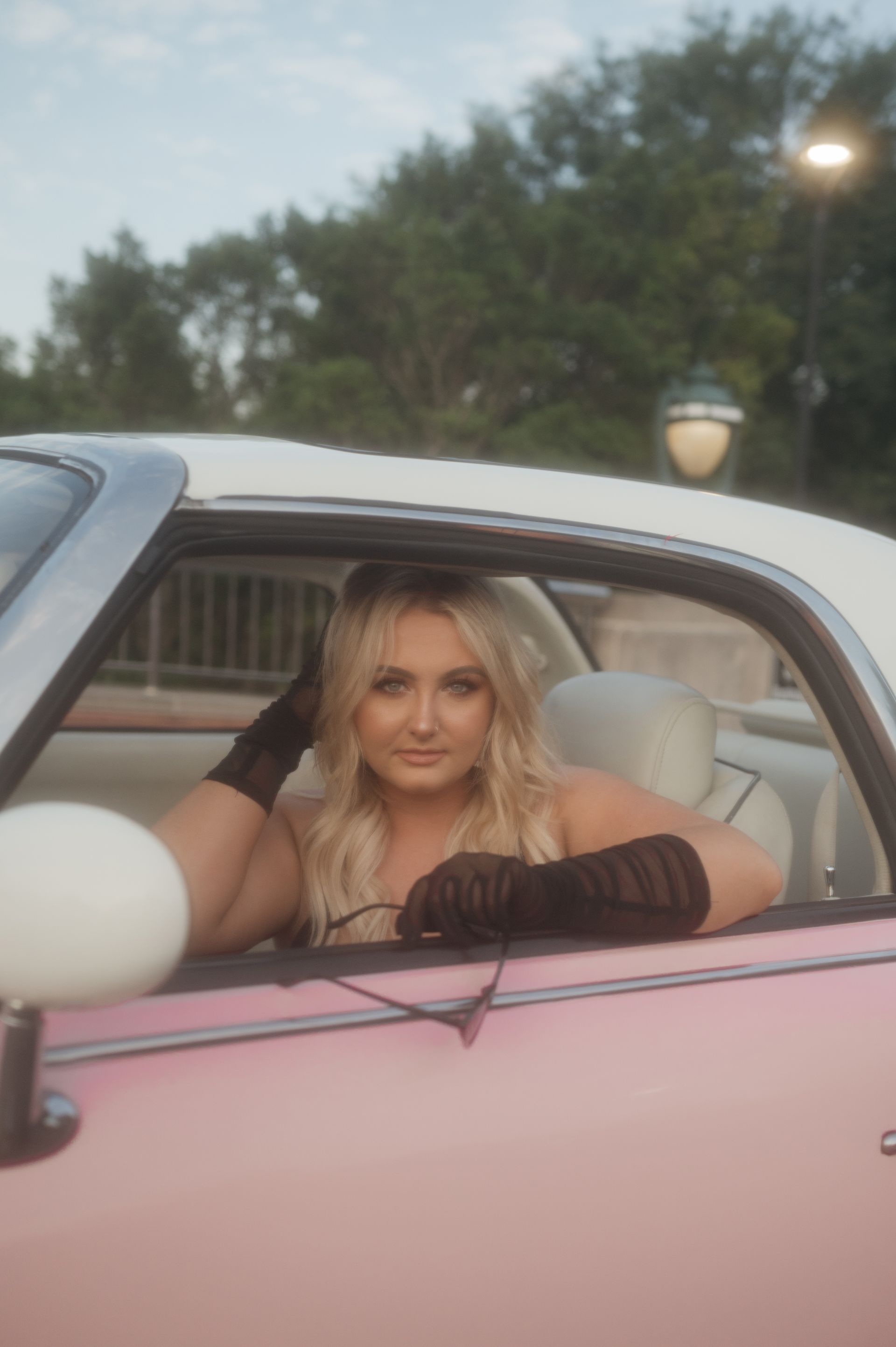 A woman is sitting in the driver 's seat of a pink car.