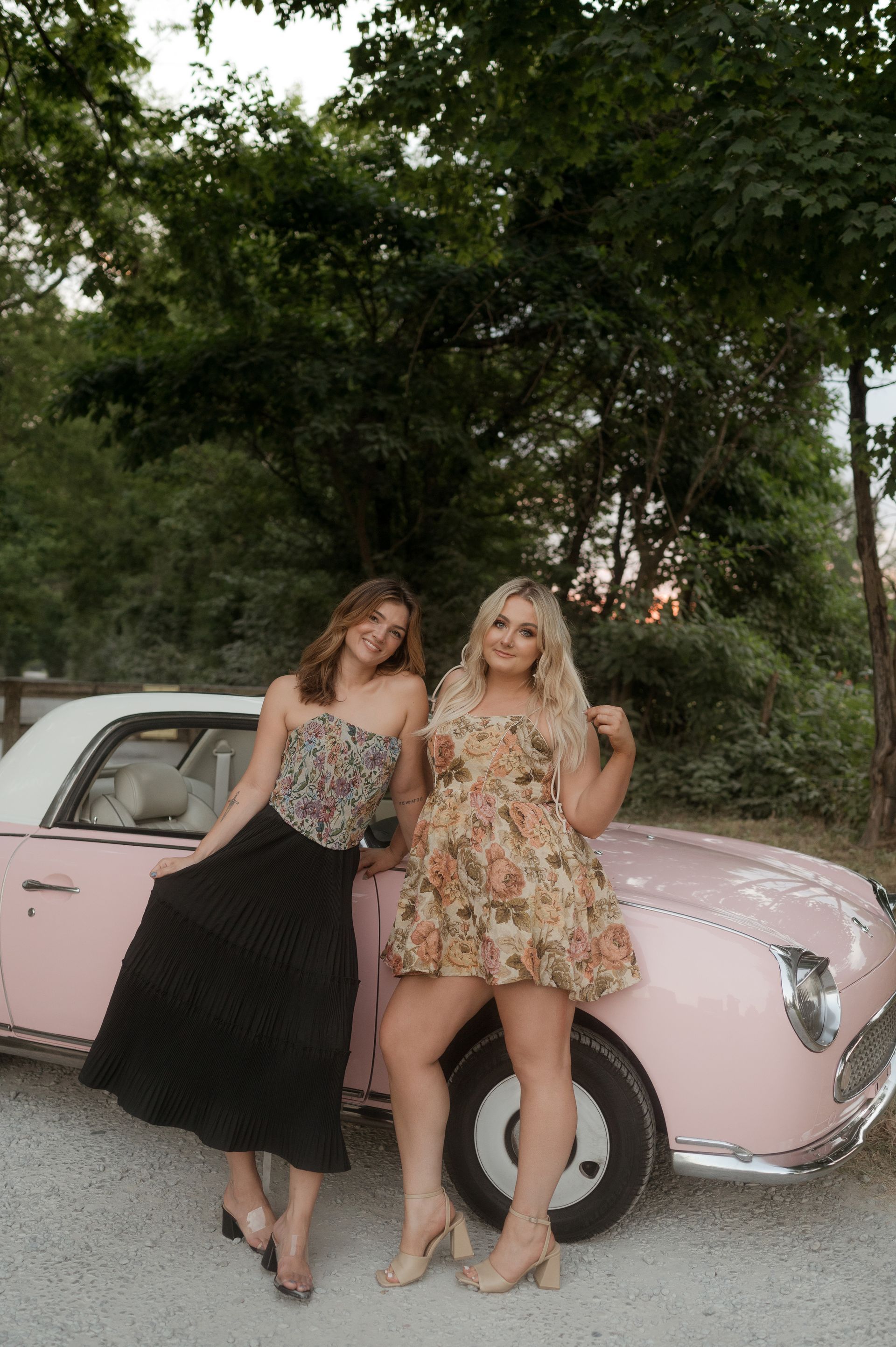 Two women are standing next to a pink car.