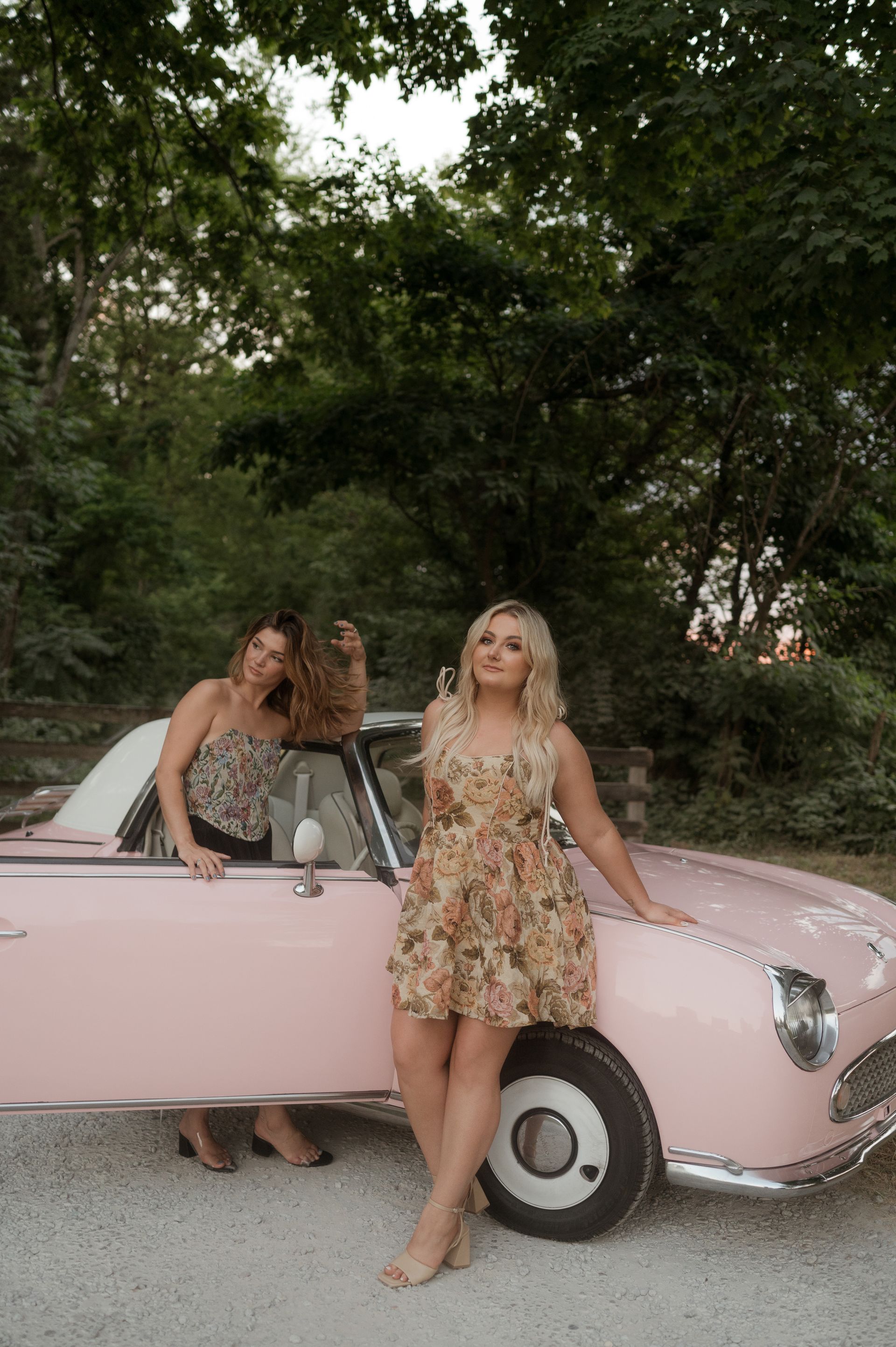 Two women are standing next to a pink car.