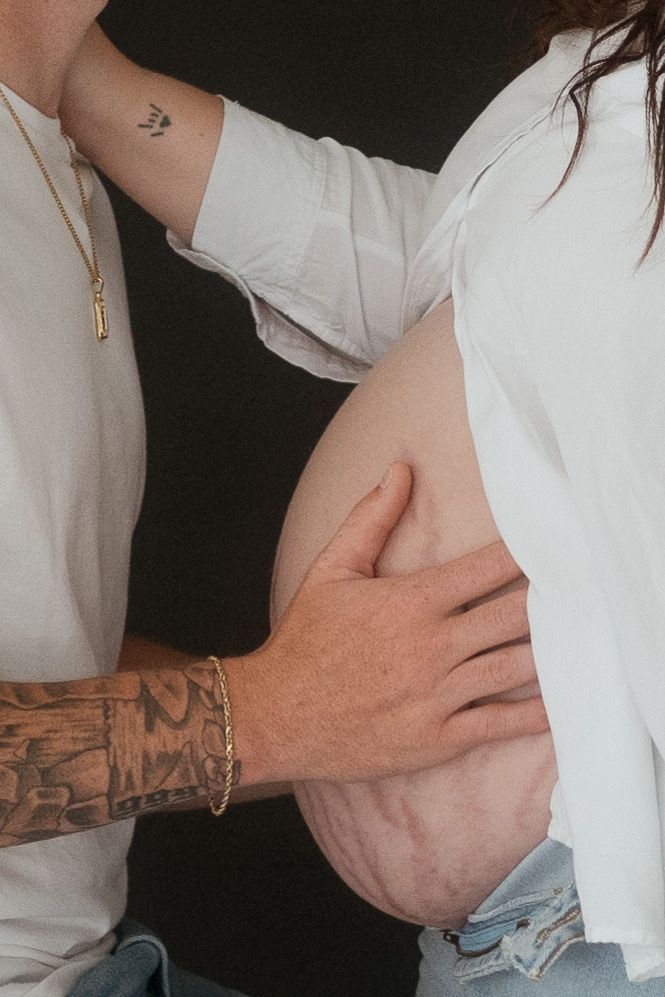 A man with a tattoo on his arm is holding a pregnant woman 's belly