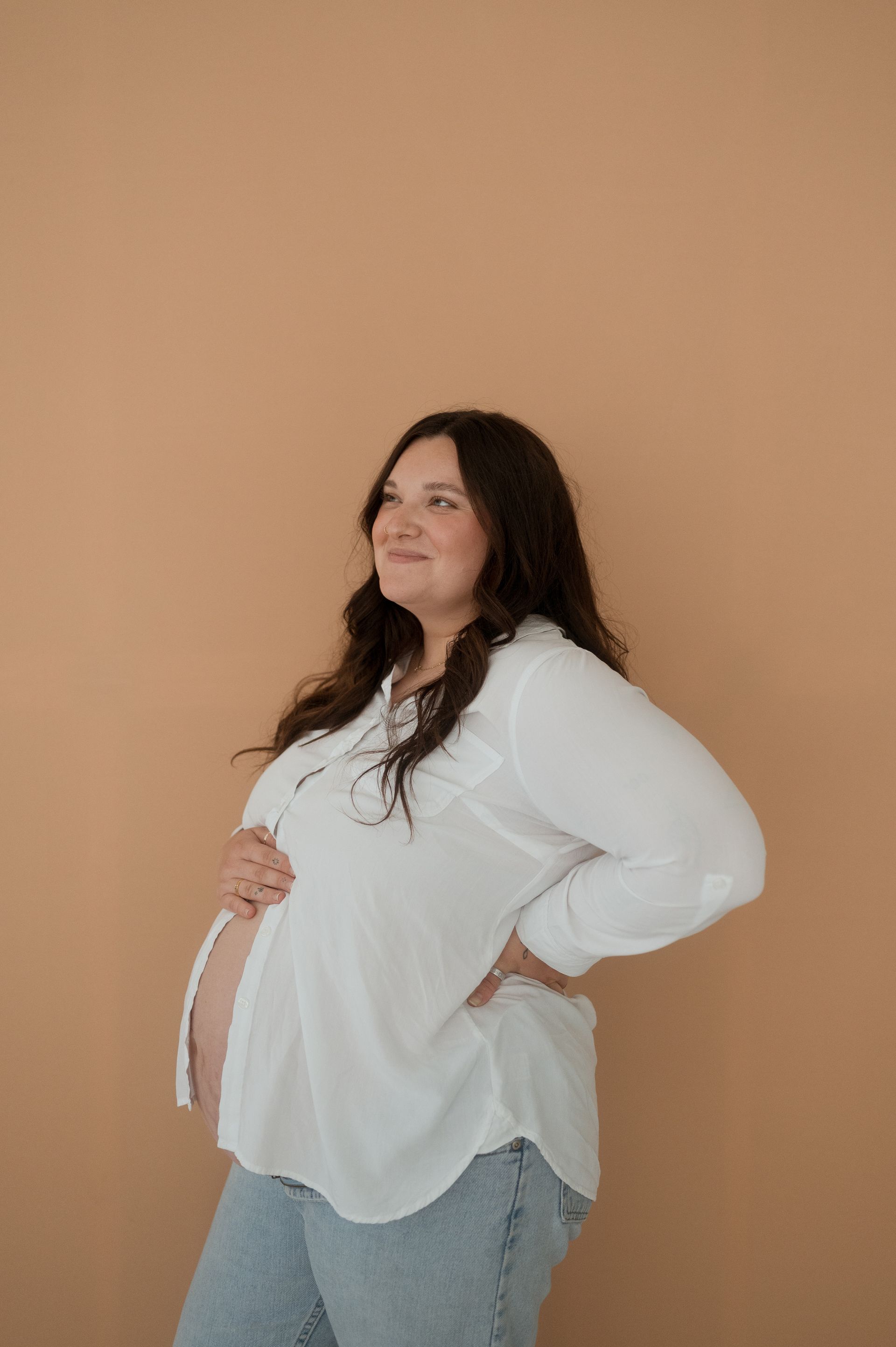 A pregnant woman in a white shirt and jeans is holding her belly.