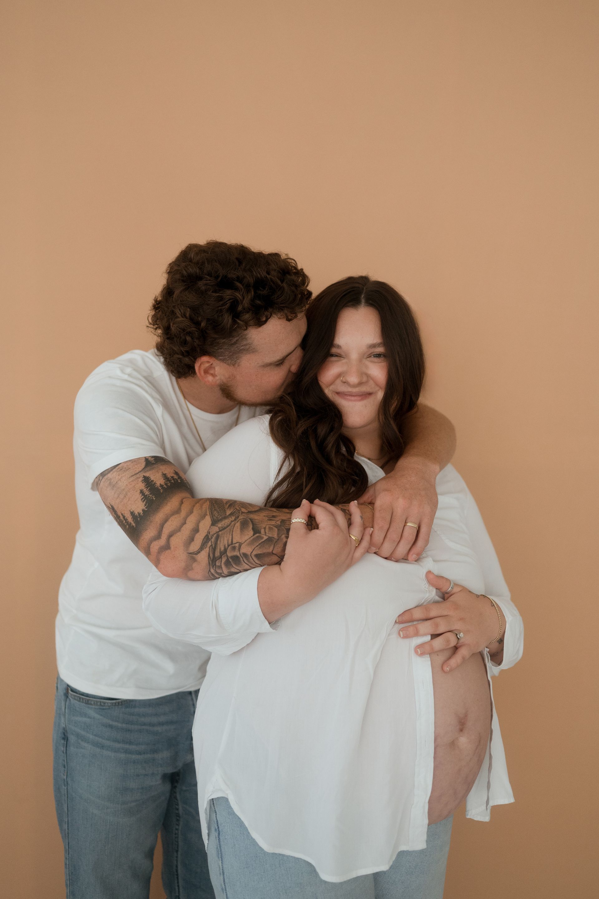 A man is kissing a pregnant woman on the cheek.