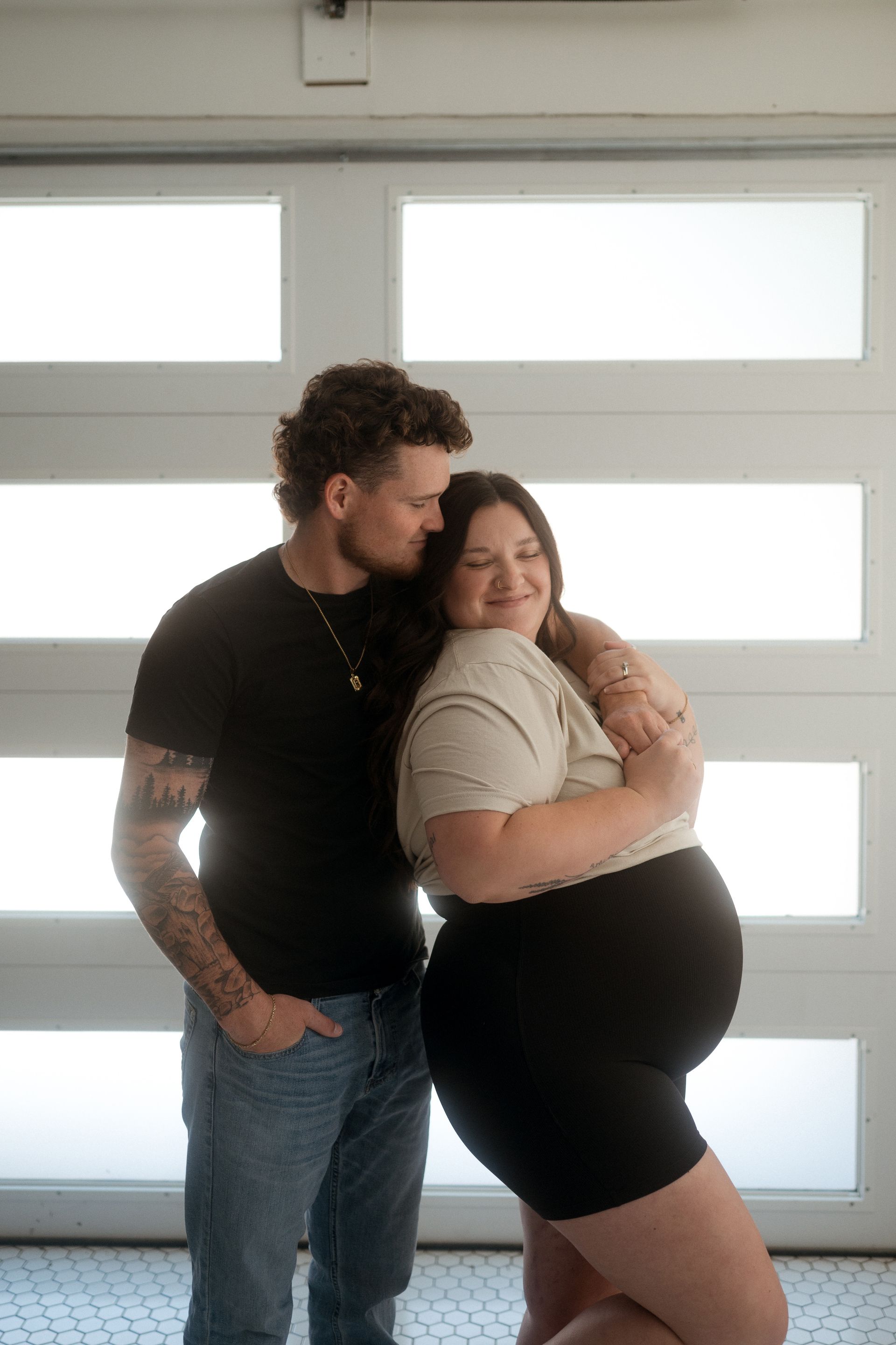 A man and a pregnant woman are standing next to each other in front of a garage door.