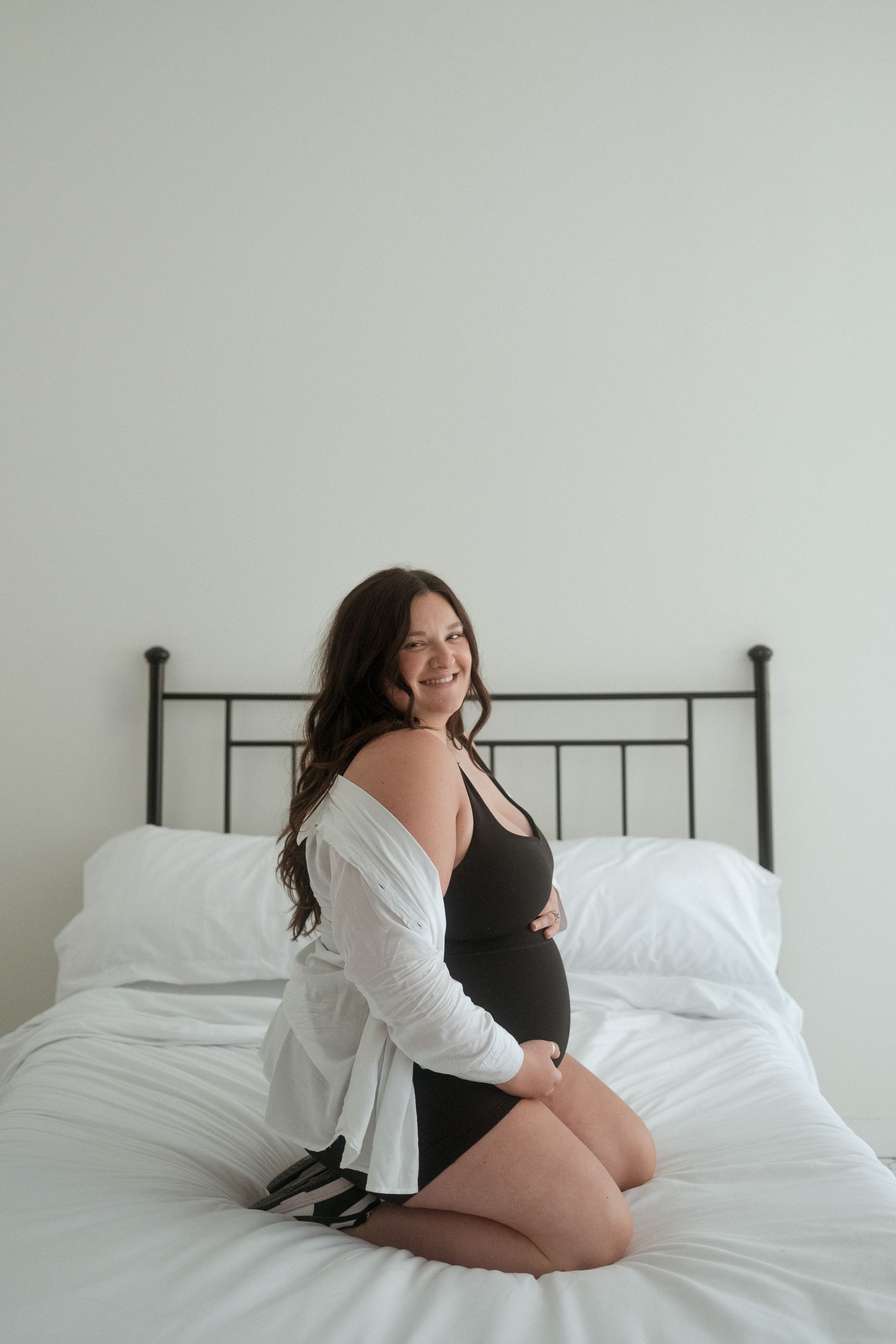 A pregnant woman is sitting on a bed holding her belly.