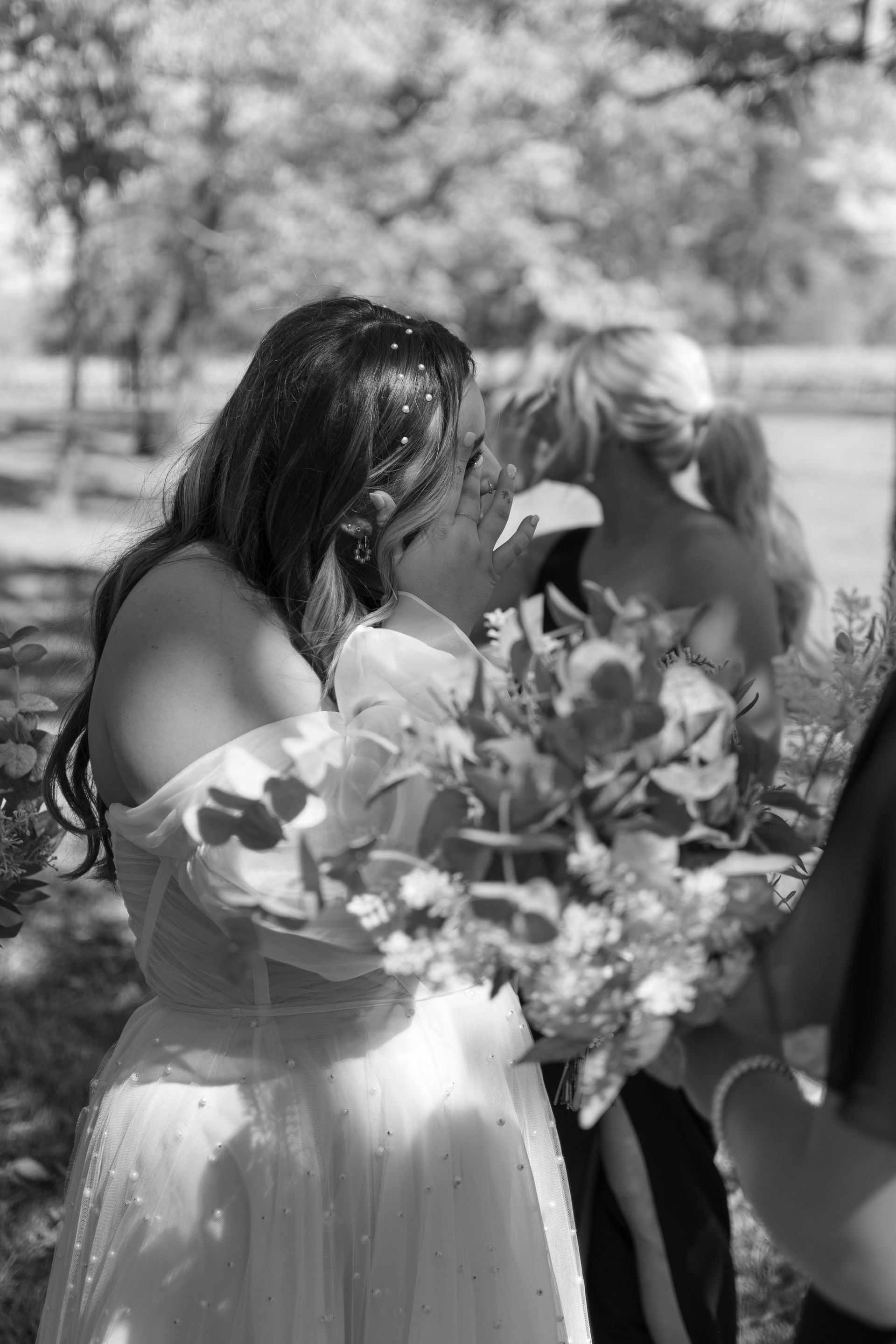 A bride and her bridesmaid are kissing in a black and white photo.