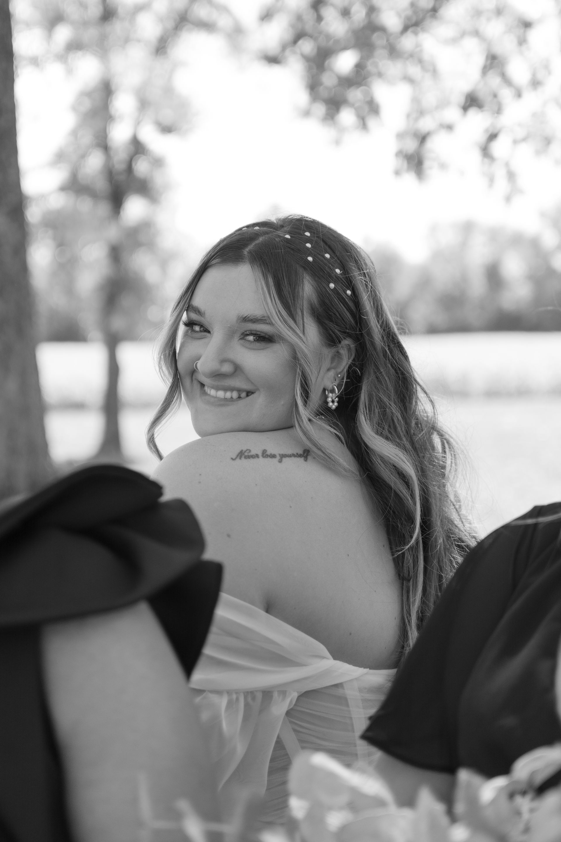 A woman with a tattoo on her back is smiling in a black and white photo.