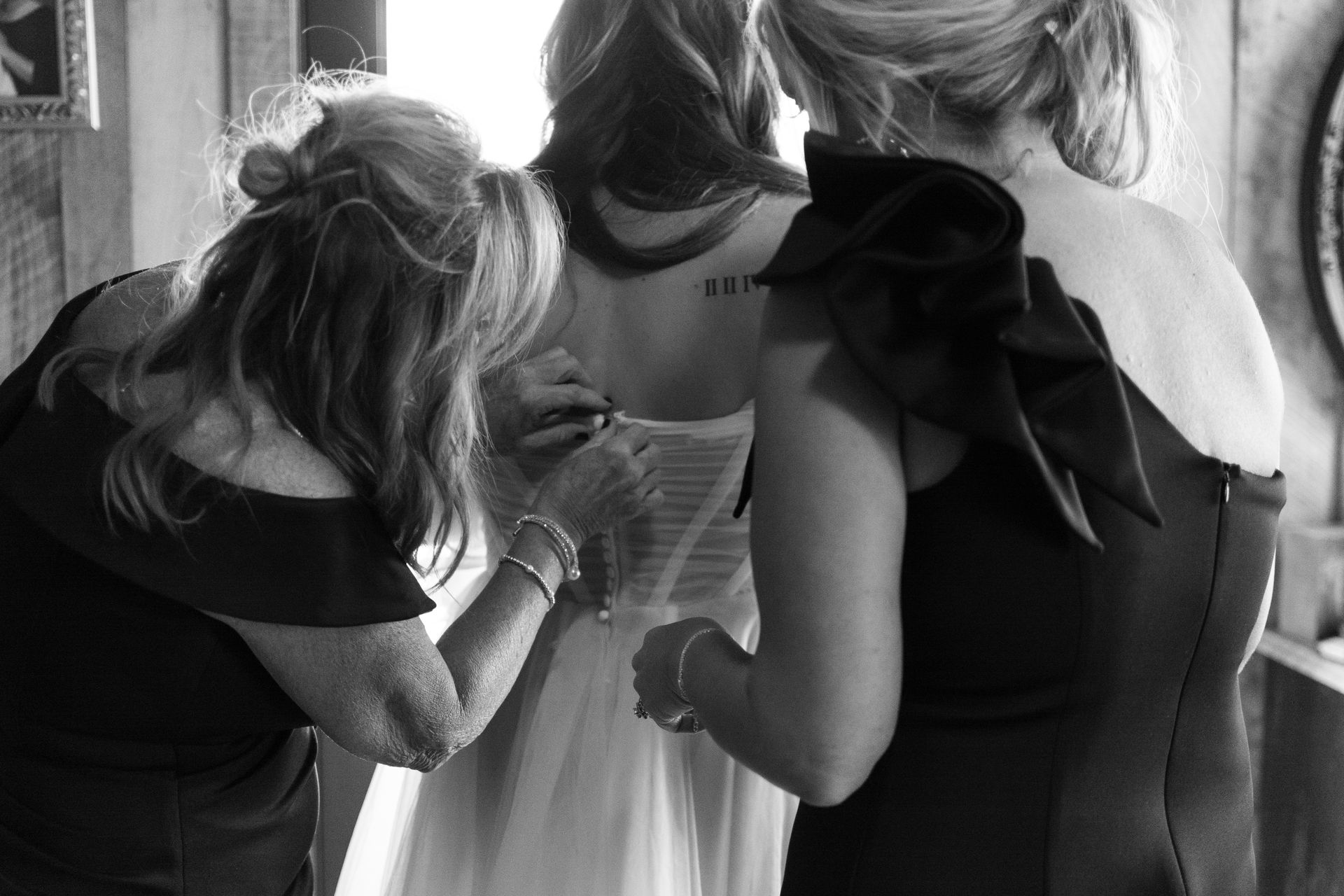 A black and white photo of two women helping a bride get ready for her wedding.