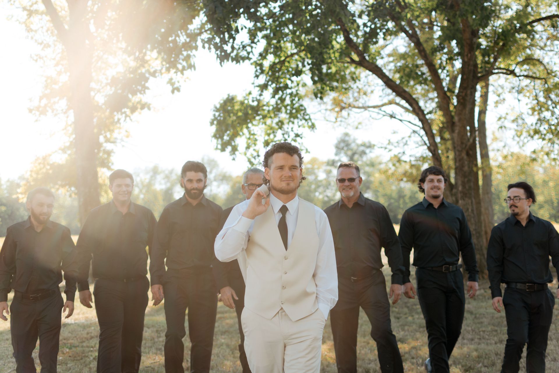 A man in a white suit is standing in front of a group of men in black shirts.