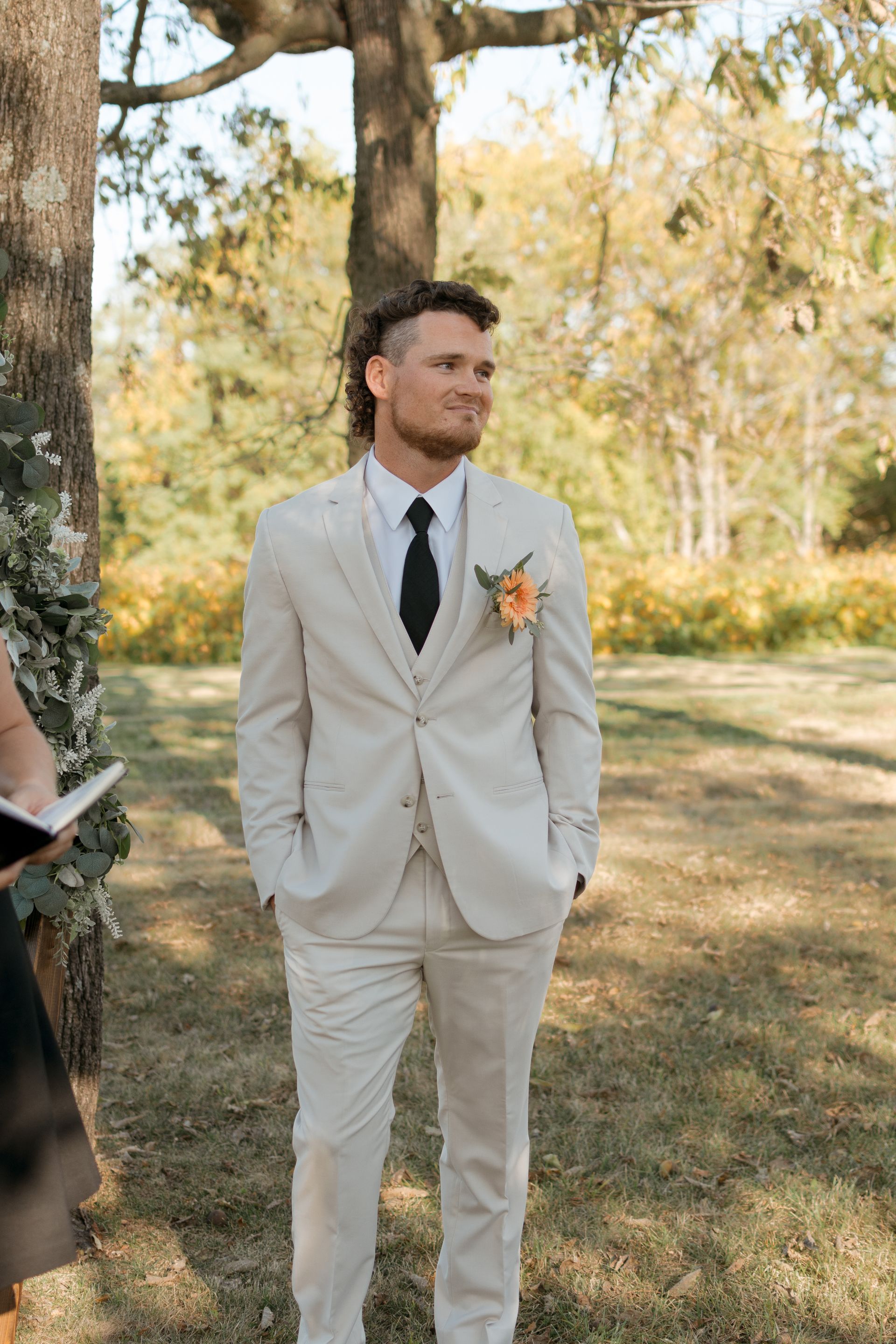 A man in a white suit and tie is standing in a field.
