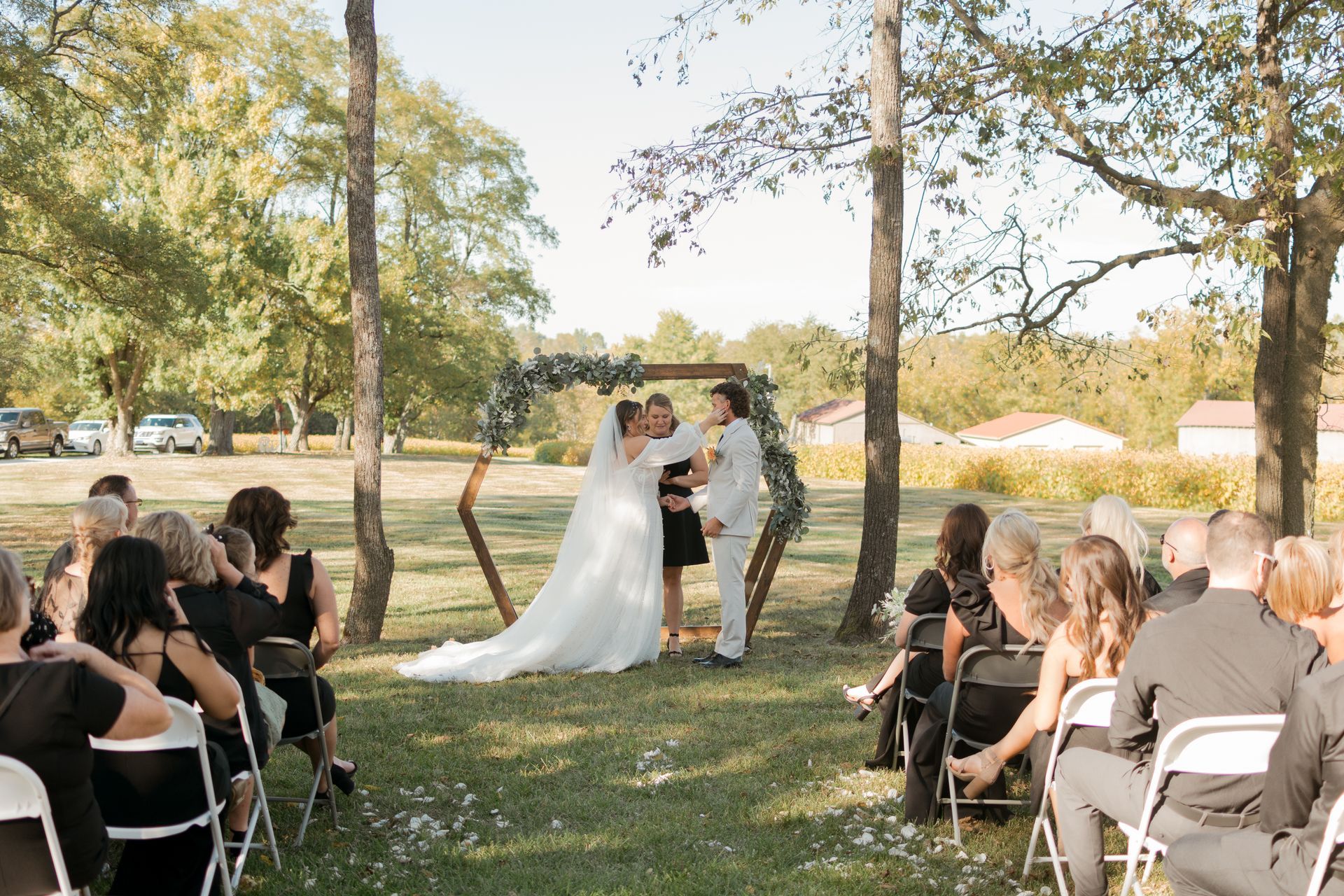 A bride and groom are kissing during their wedding ceremony while their guests watch.
