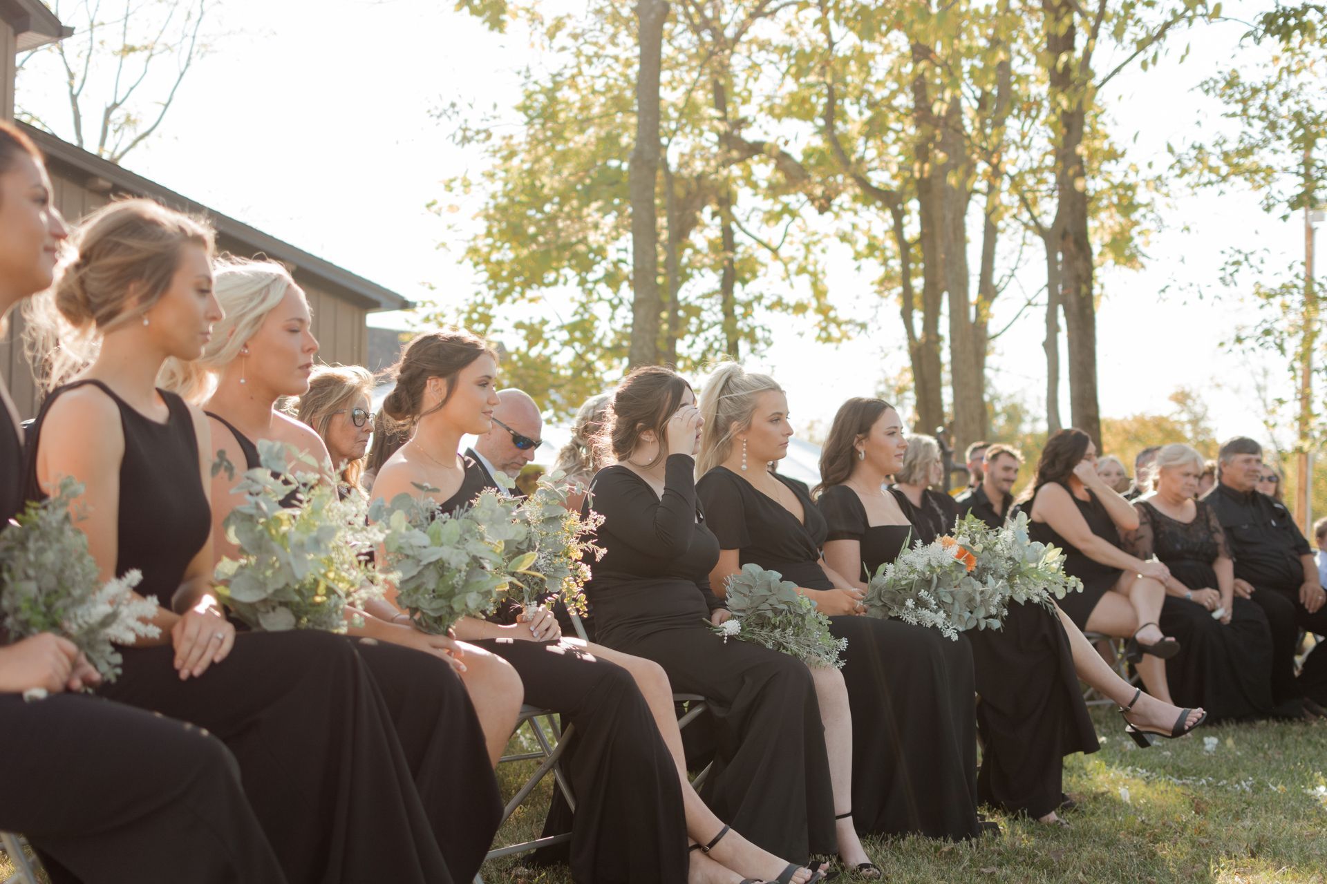 A group of women in black dresses are sitting in a row in a field.
