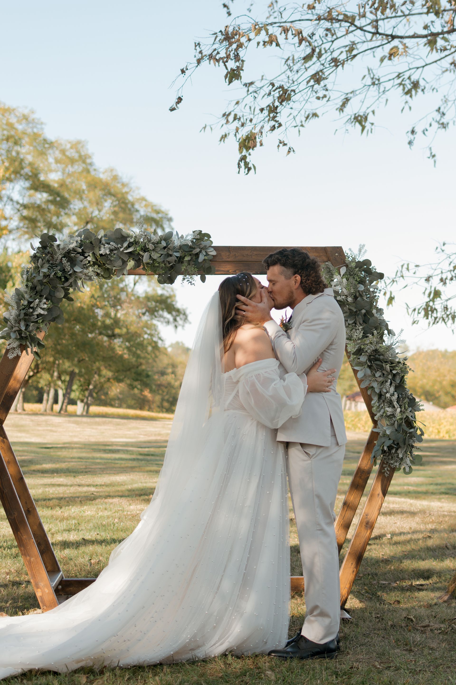 A bride and groom are kissing under a wooden arch.