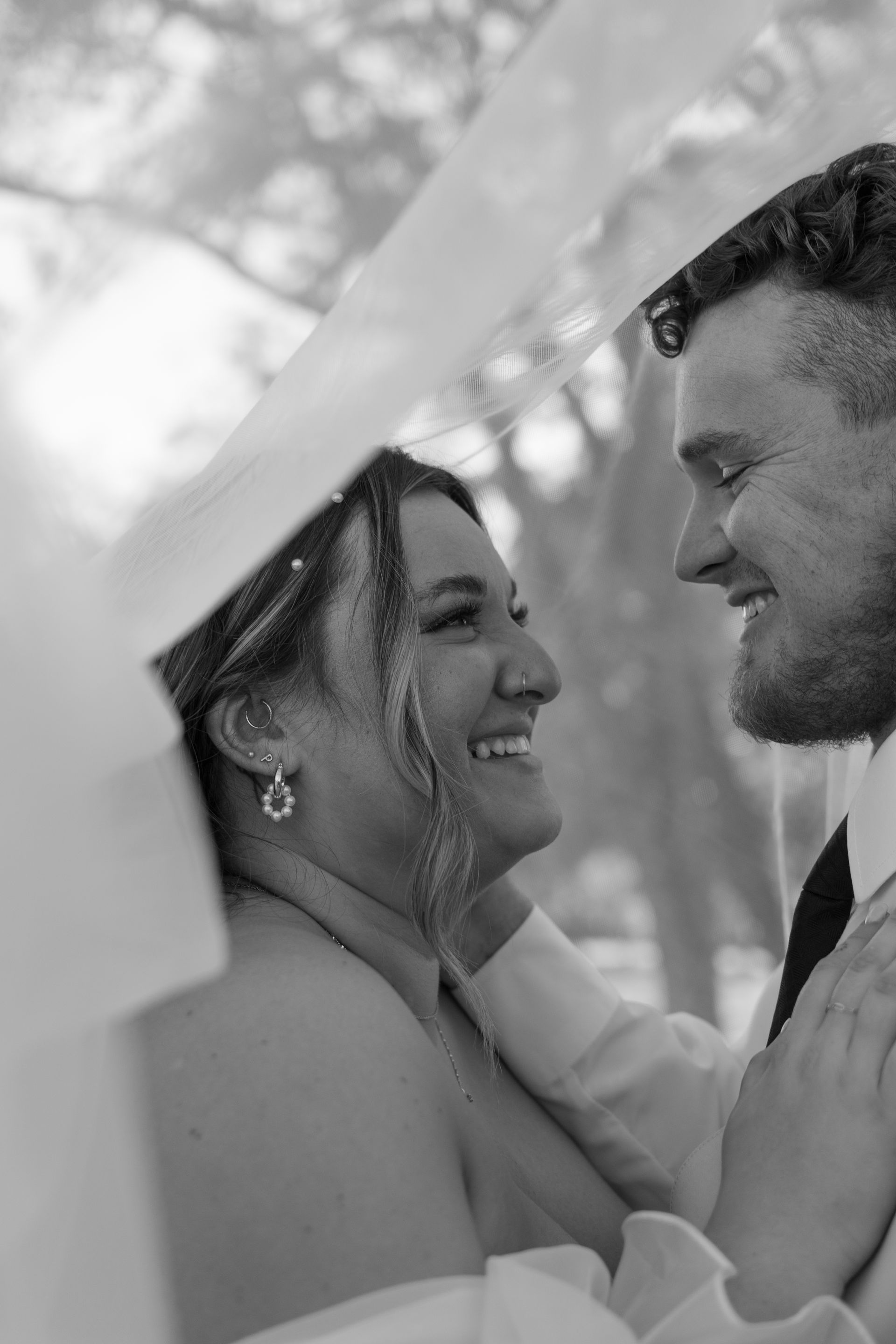 A black and white photo of a bride and groom looking at each other under an umbrella.