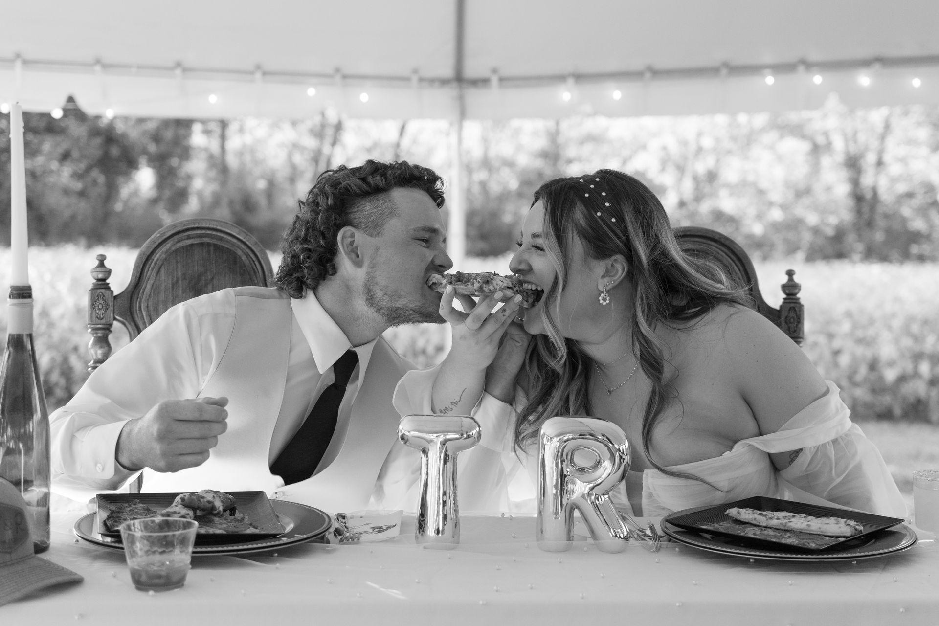 A bride and groom are sitting at a table under a tent eating food.