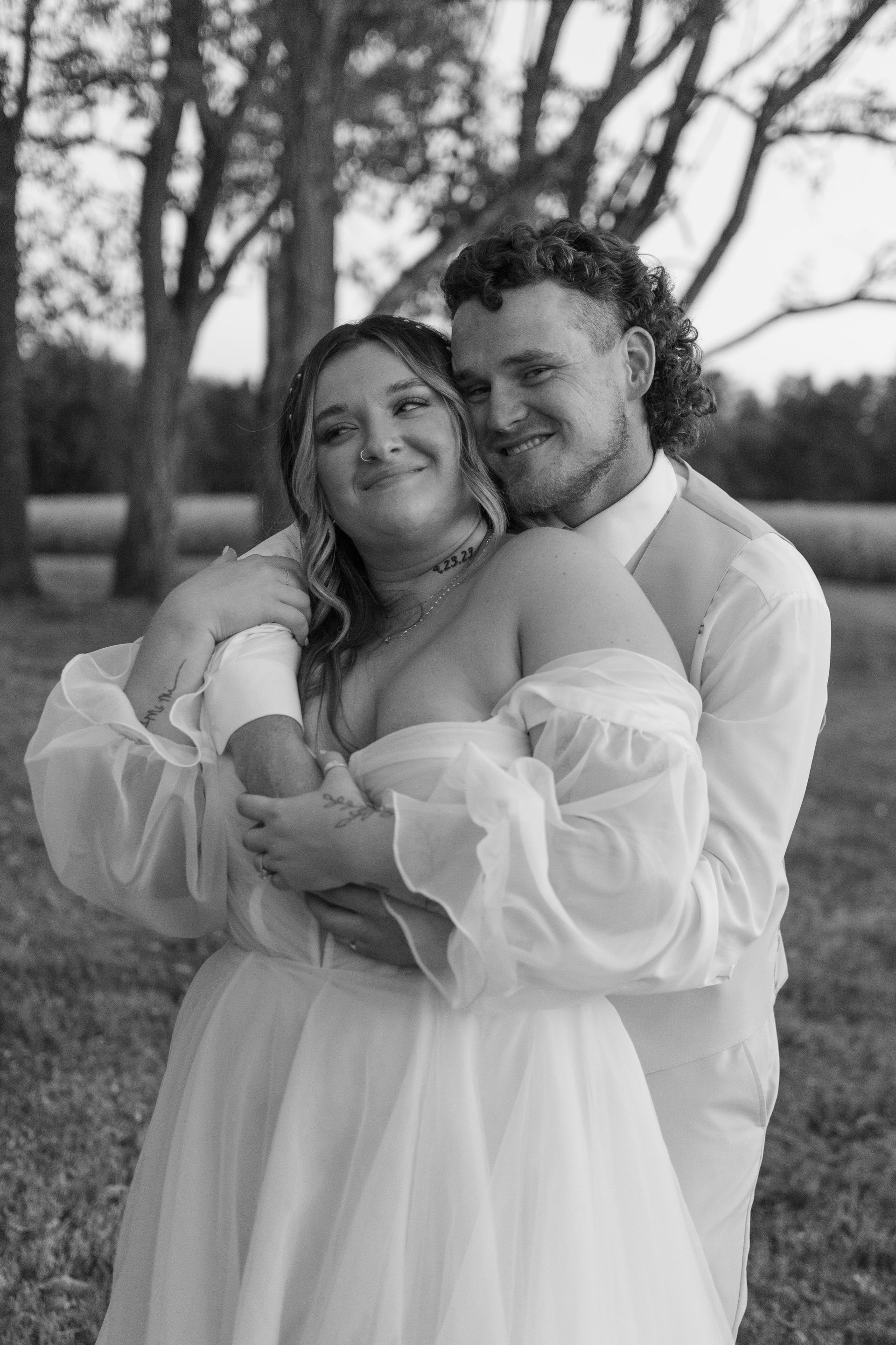 A black and white photo of a bride and groom hugging each other in a field.