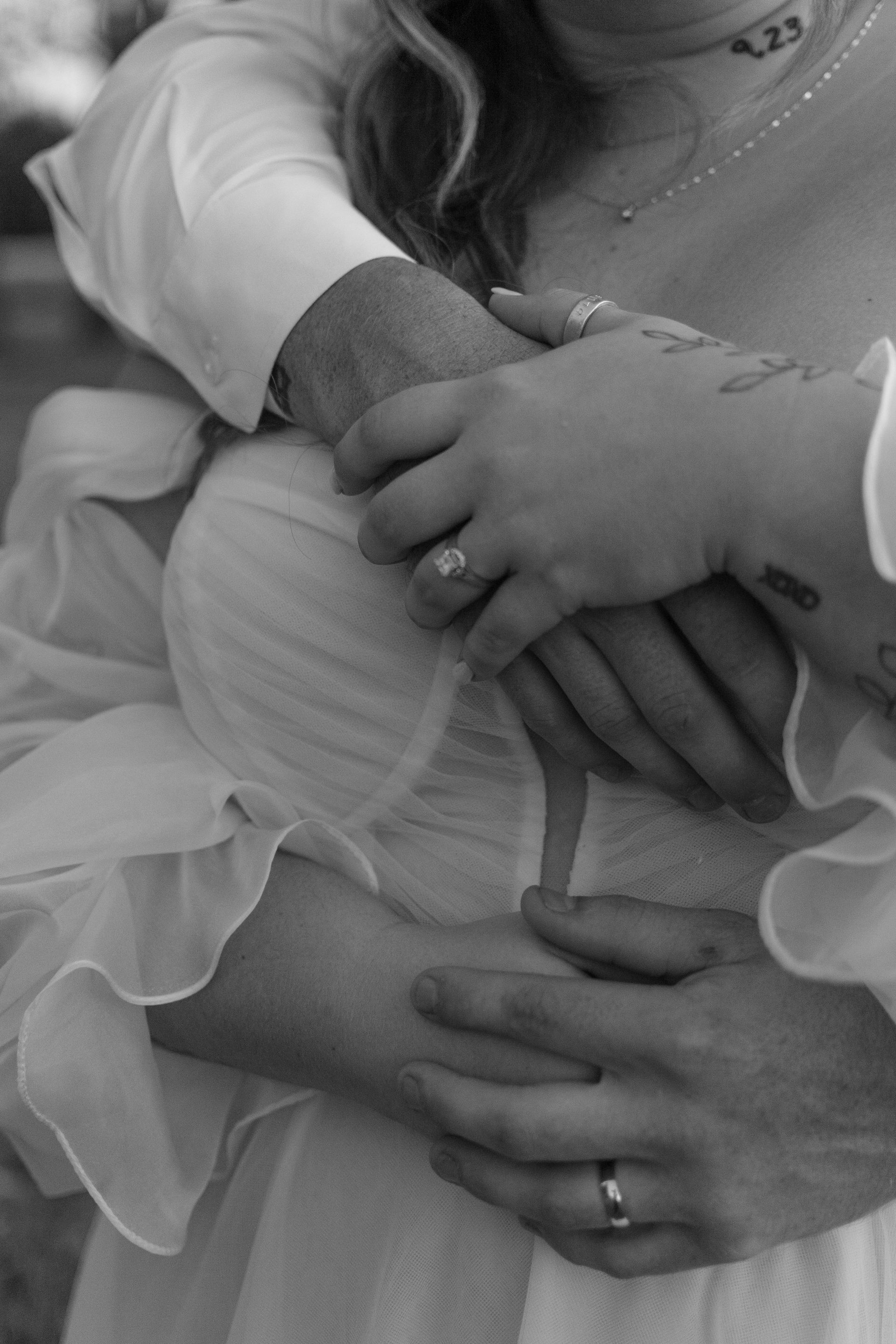 A black and white photo of a bride and groom hugging each other . the bride is wearing a wedding ring.