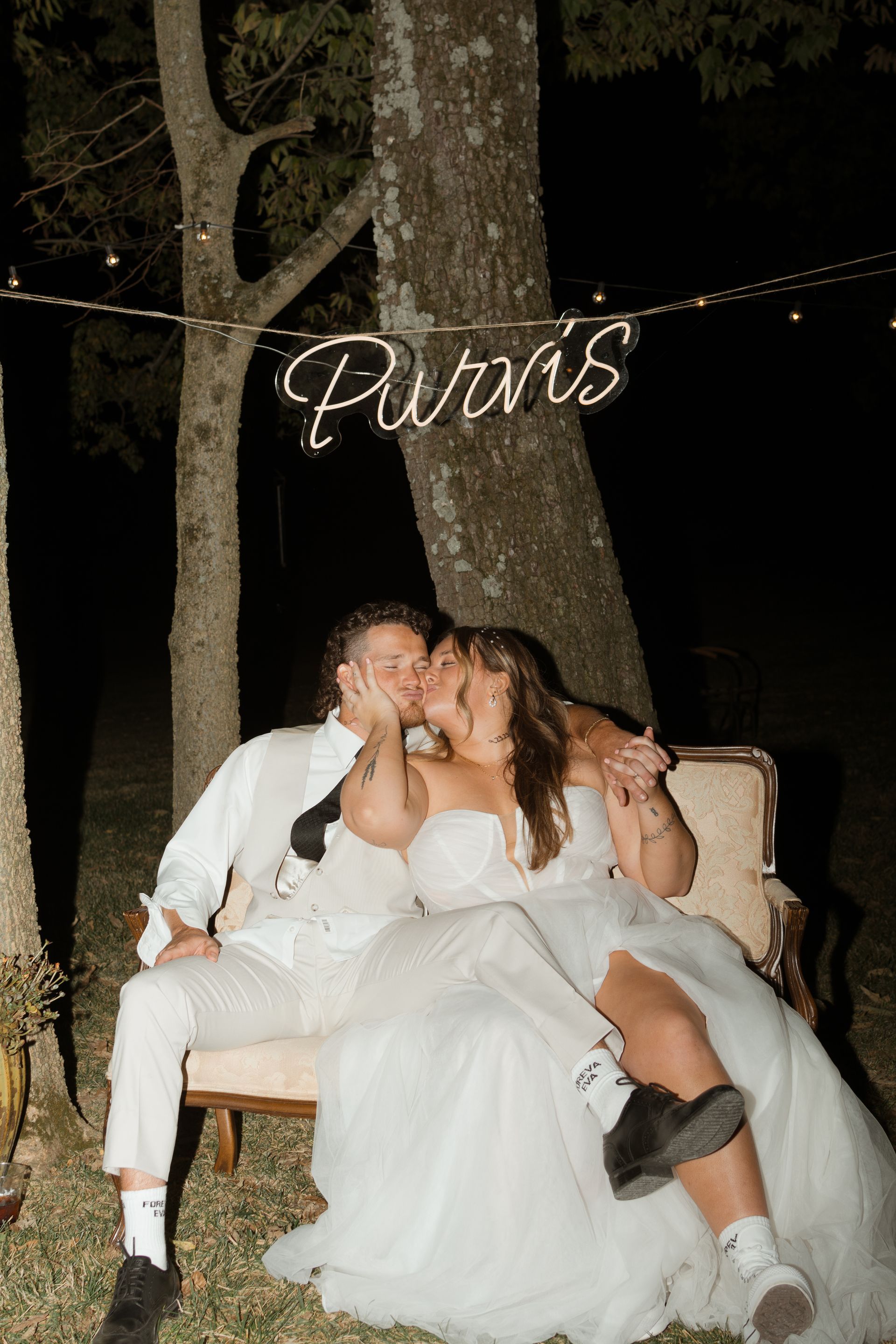 A bride and groom are kissing on a couch under a sign that says purvis.