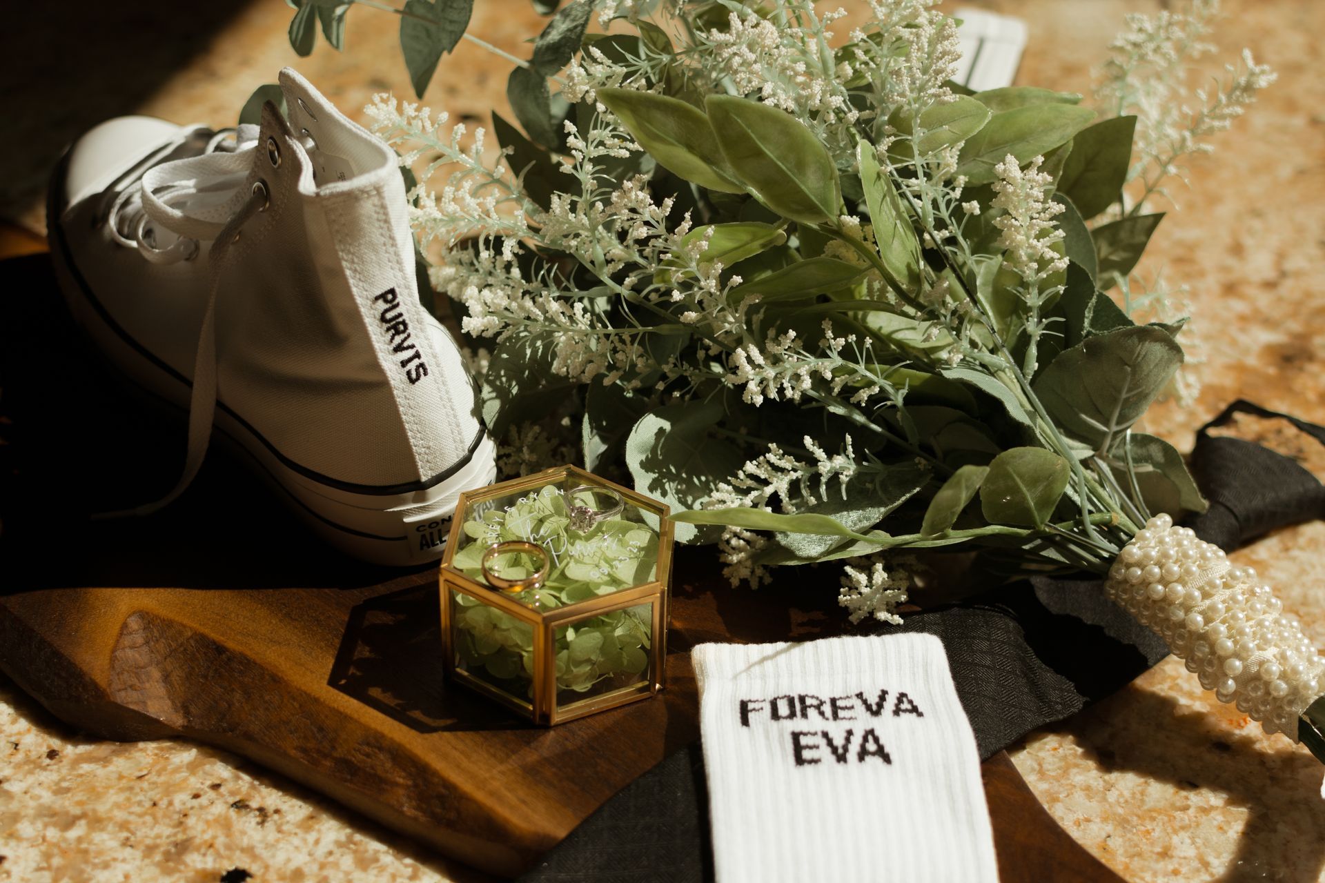 A pair of white sneakers sitting on top of a wooden table next to a bouquet of flowers.