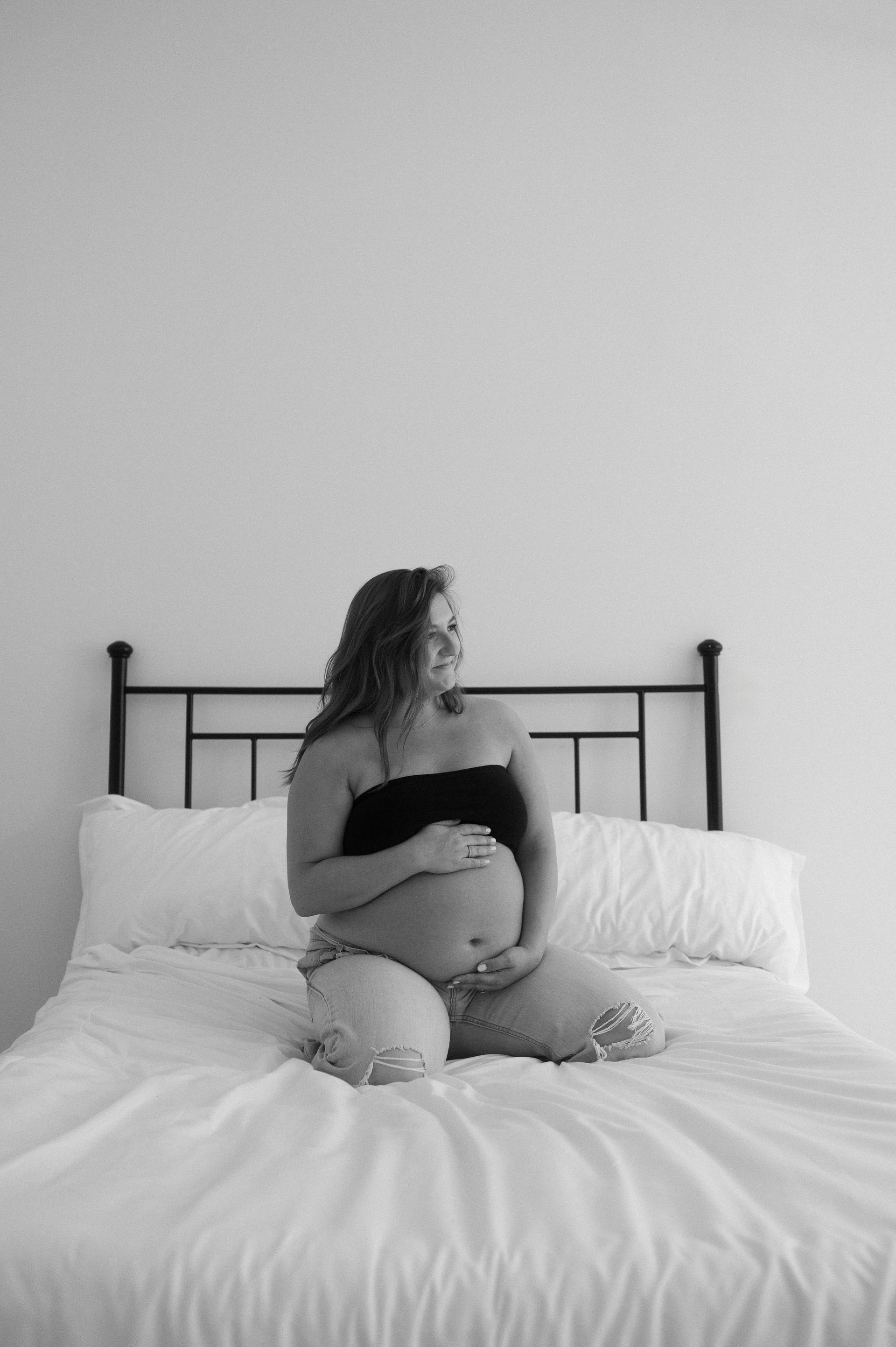 A pregnant woman is sitting on a bed in a black and white photo.