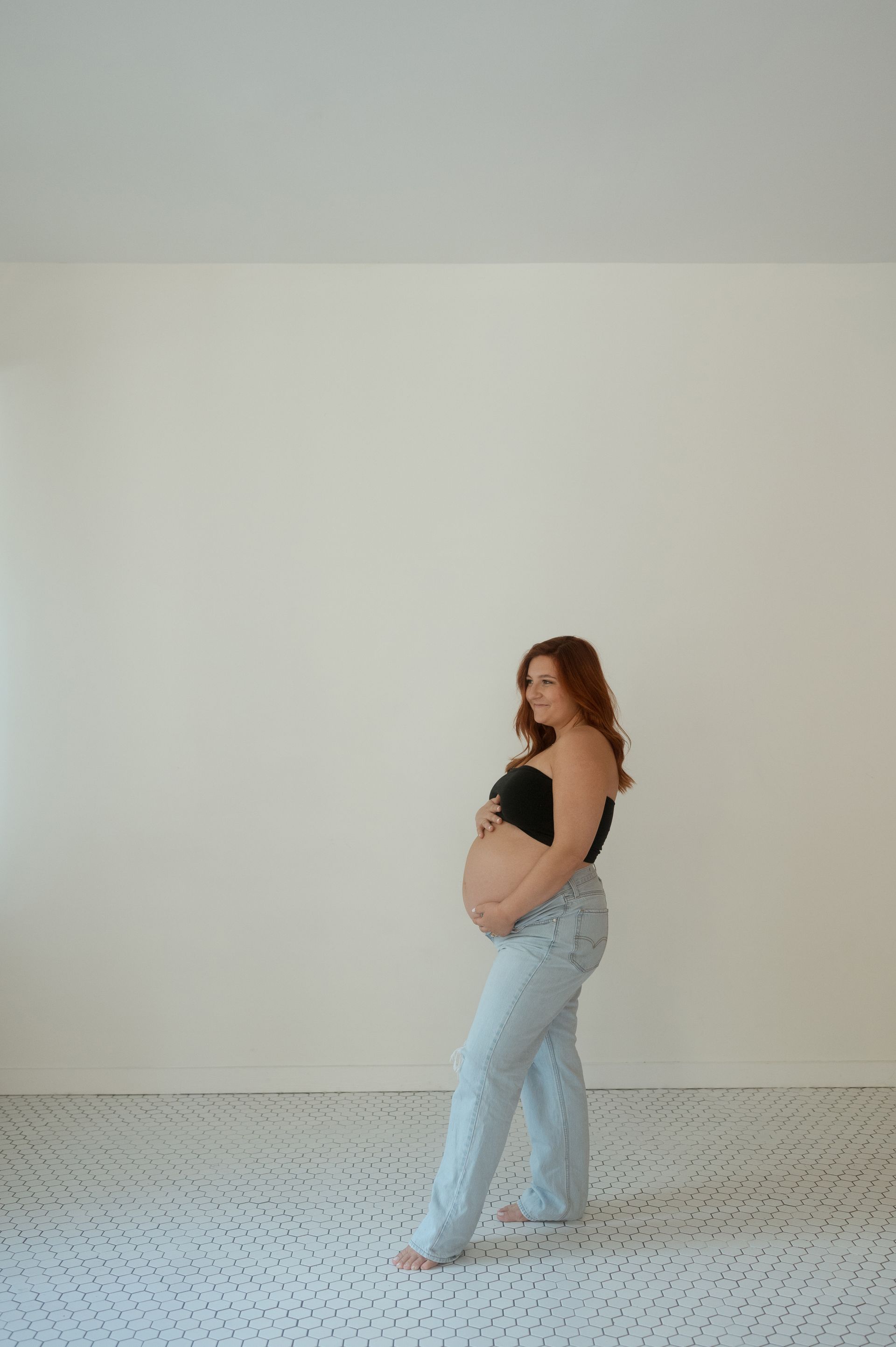 A pregnant woman is standing in an empty room holding her belly.