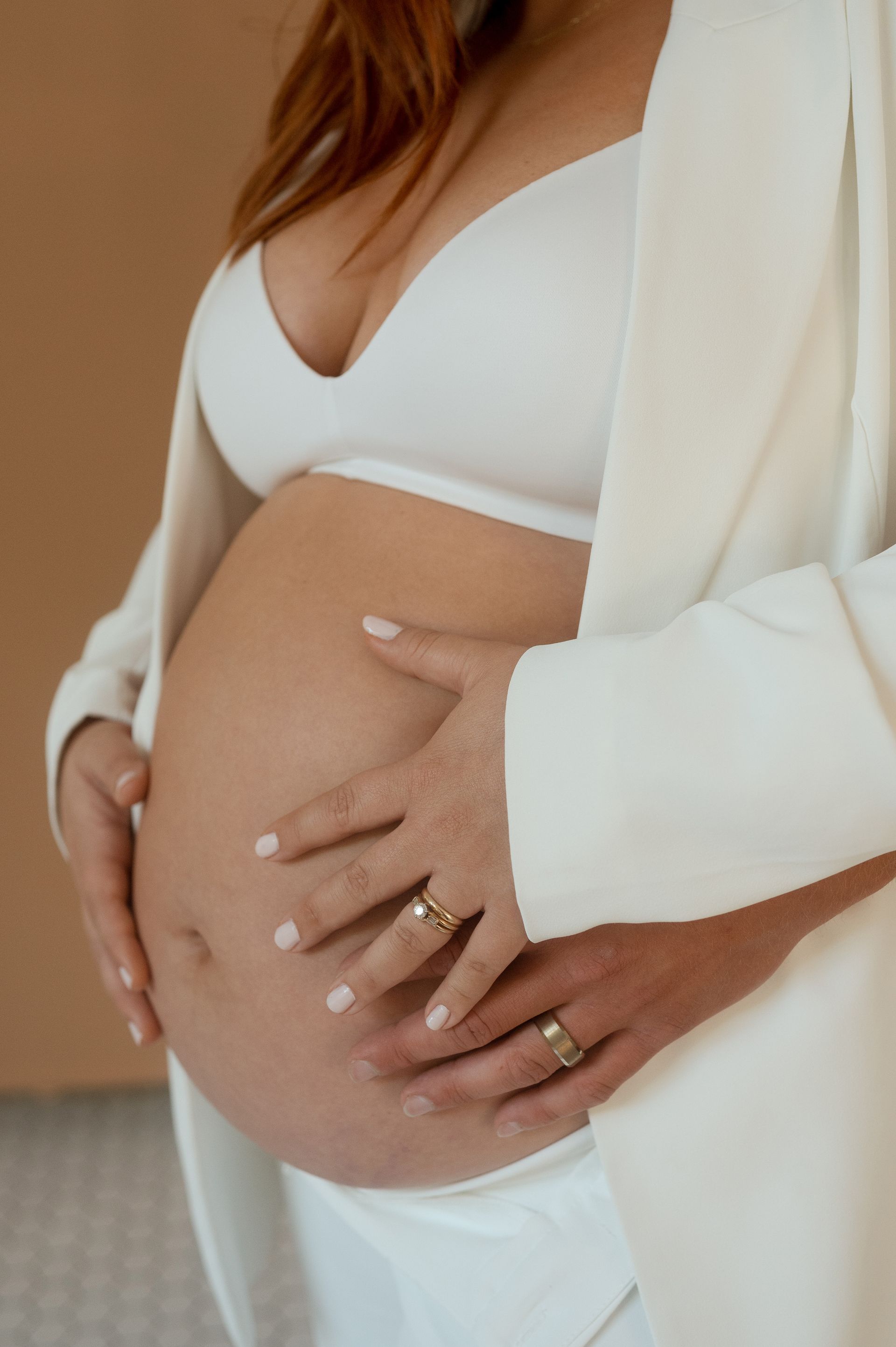 A pregnant woman in a white bra and jacket is holding her belly.