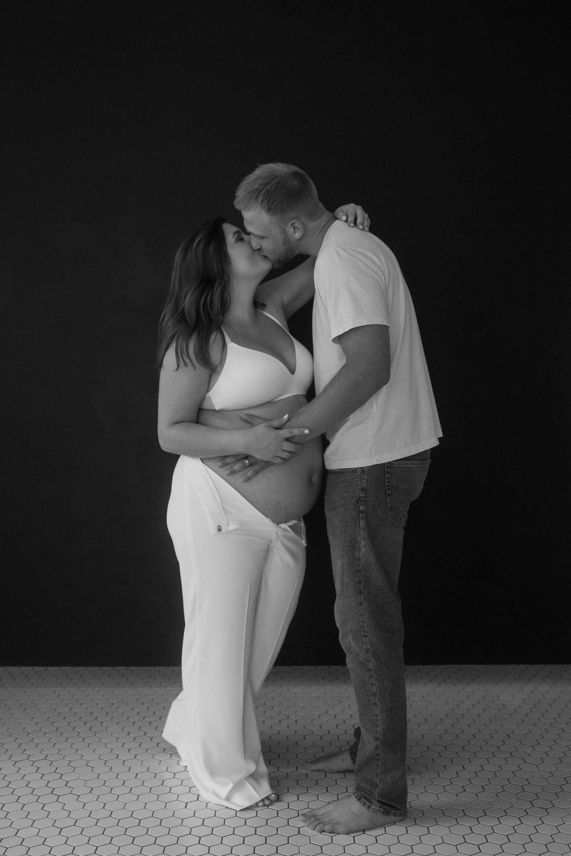 A man and a pregnant woman are kissing in a black and white photo.