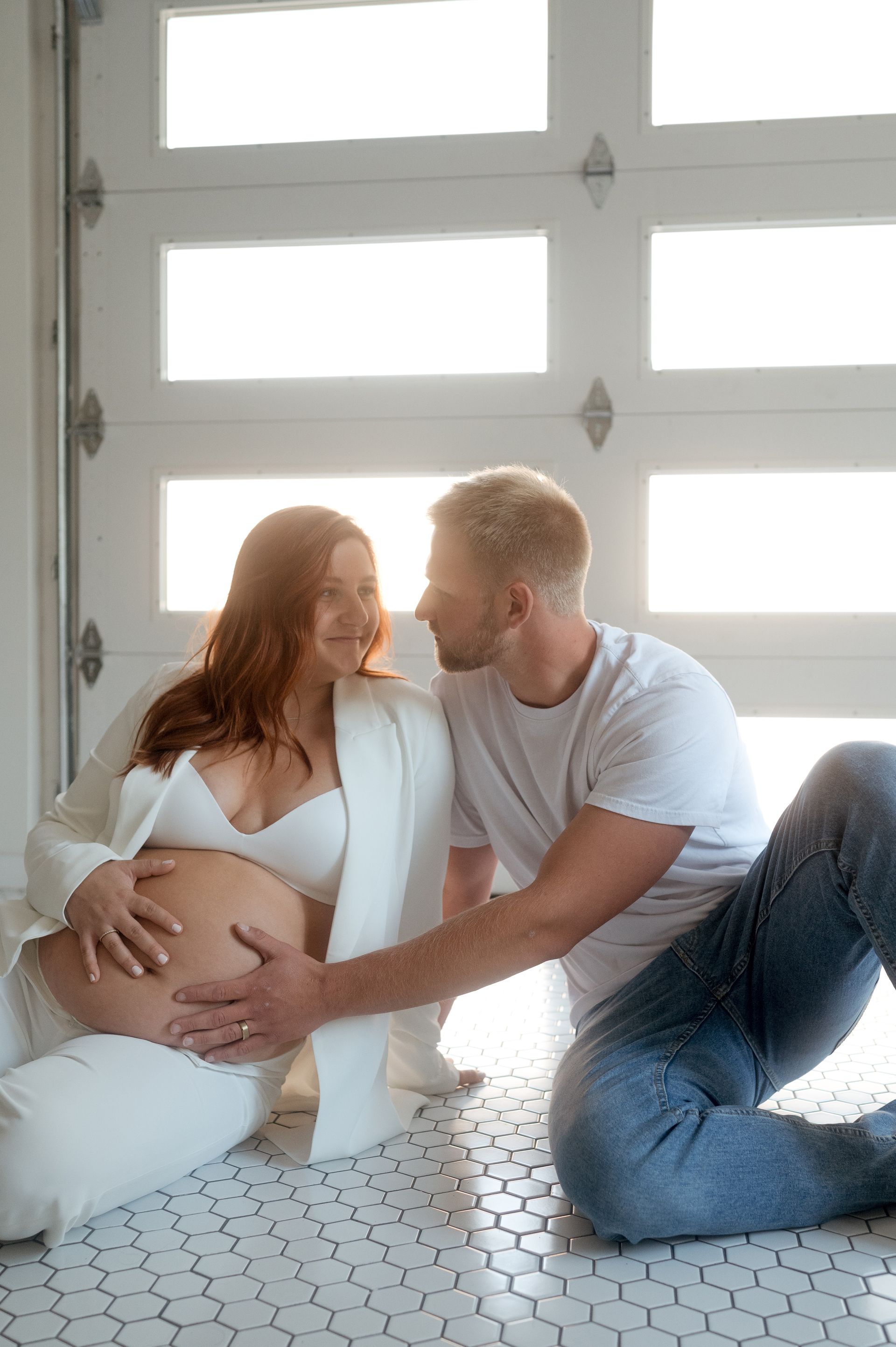 A man and a pregnant woman are sitting on the floor in front of a garage door.