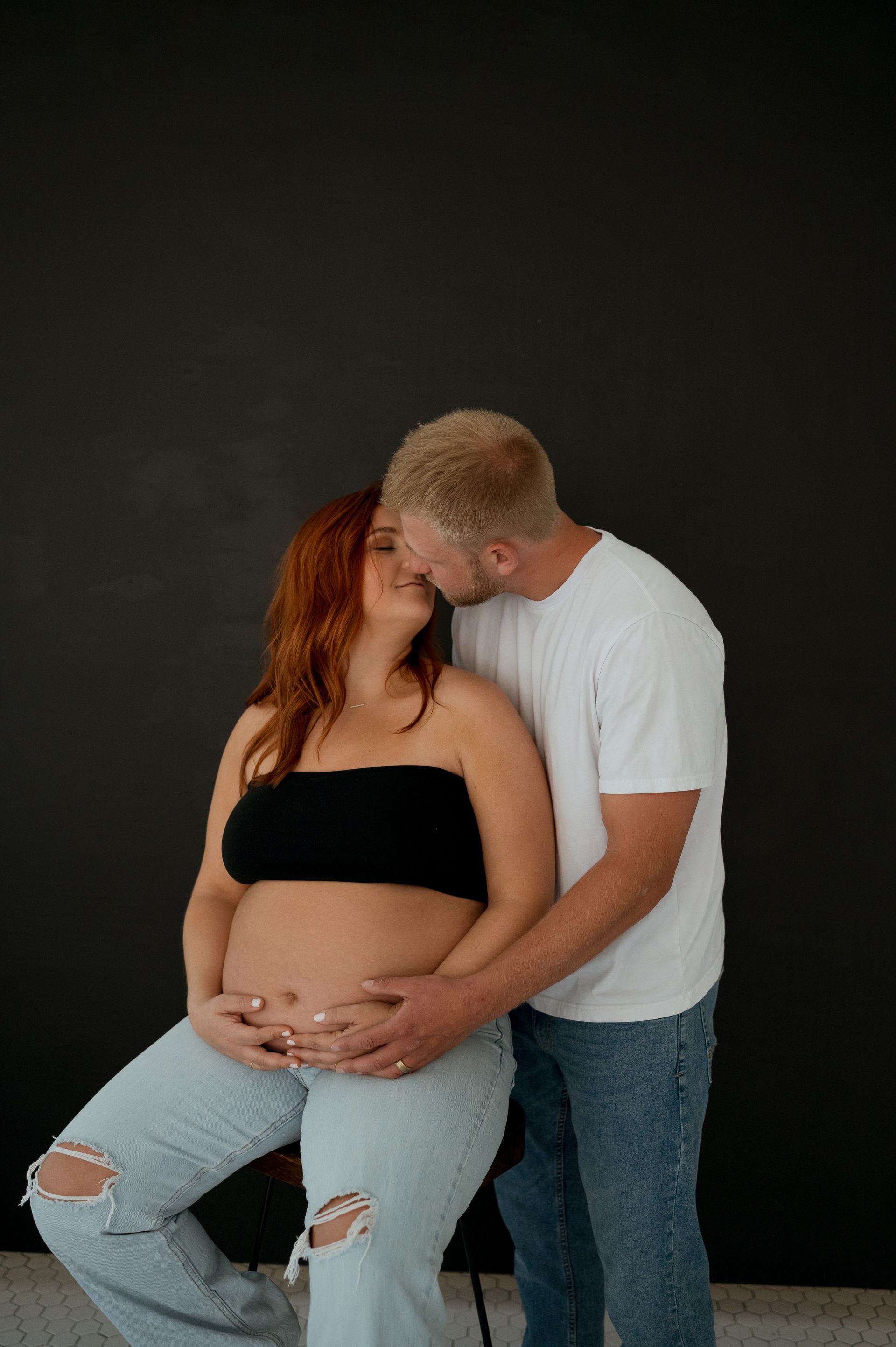 A man is kissing a pregnant woman on the cheek.