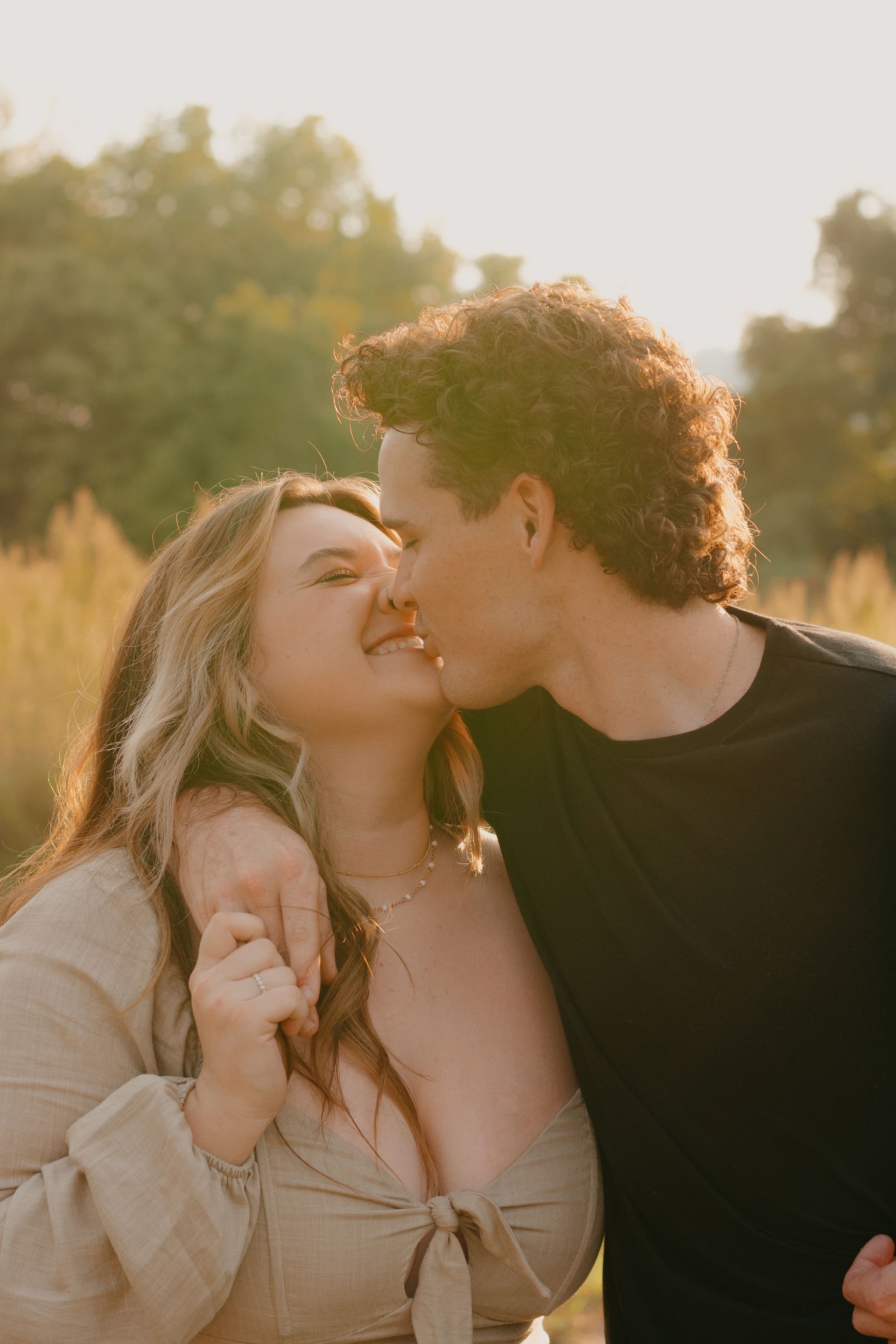 A man is kissing a woman on the cheek in a field.
