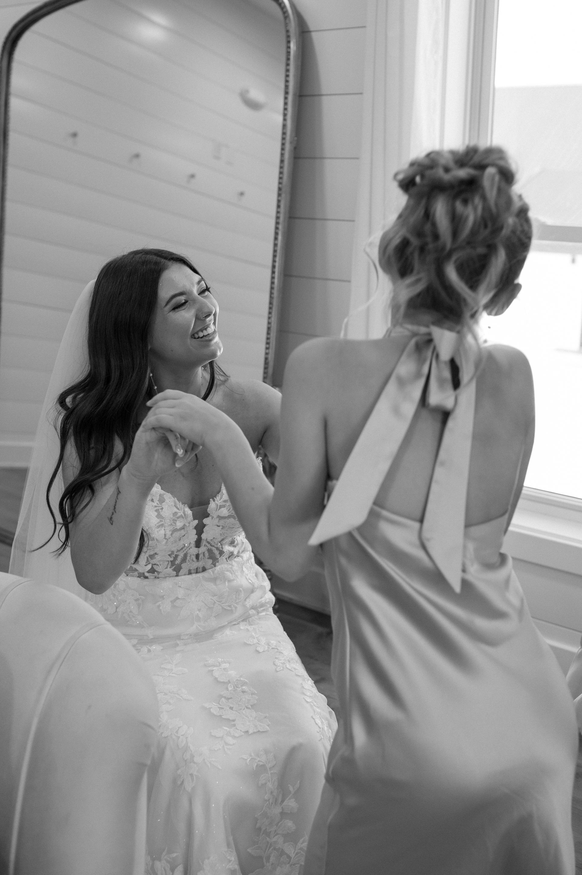 A bride and her bridesmaid are looking at themselves in a mirror.