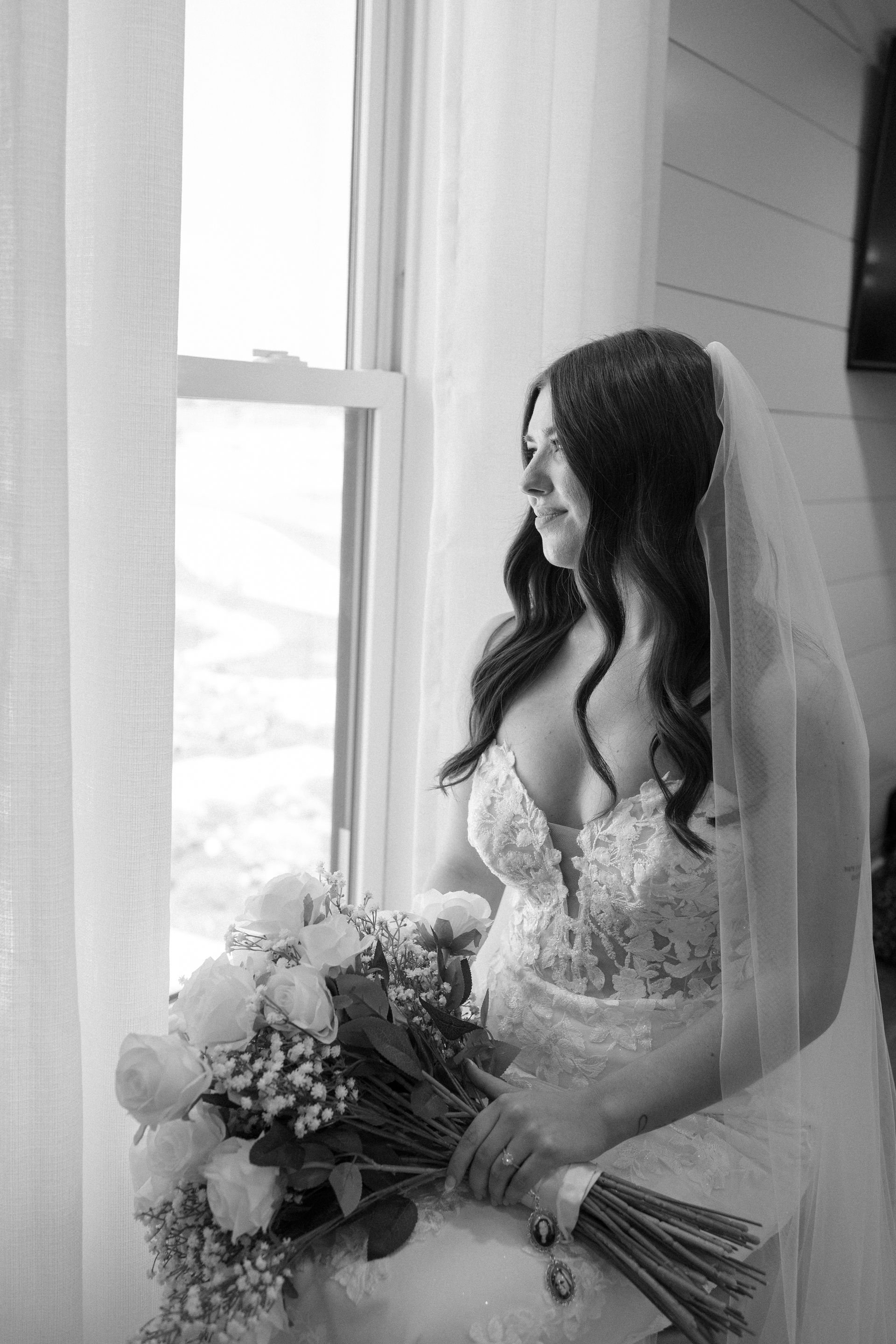 The bride is holding a bouquet of flowers and looking out the window.