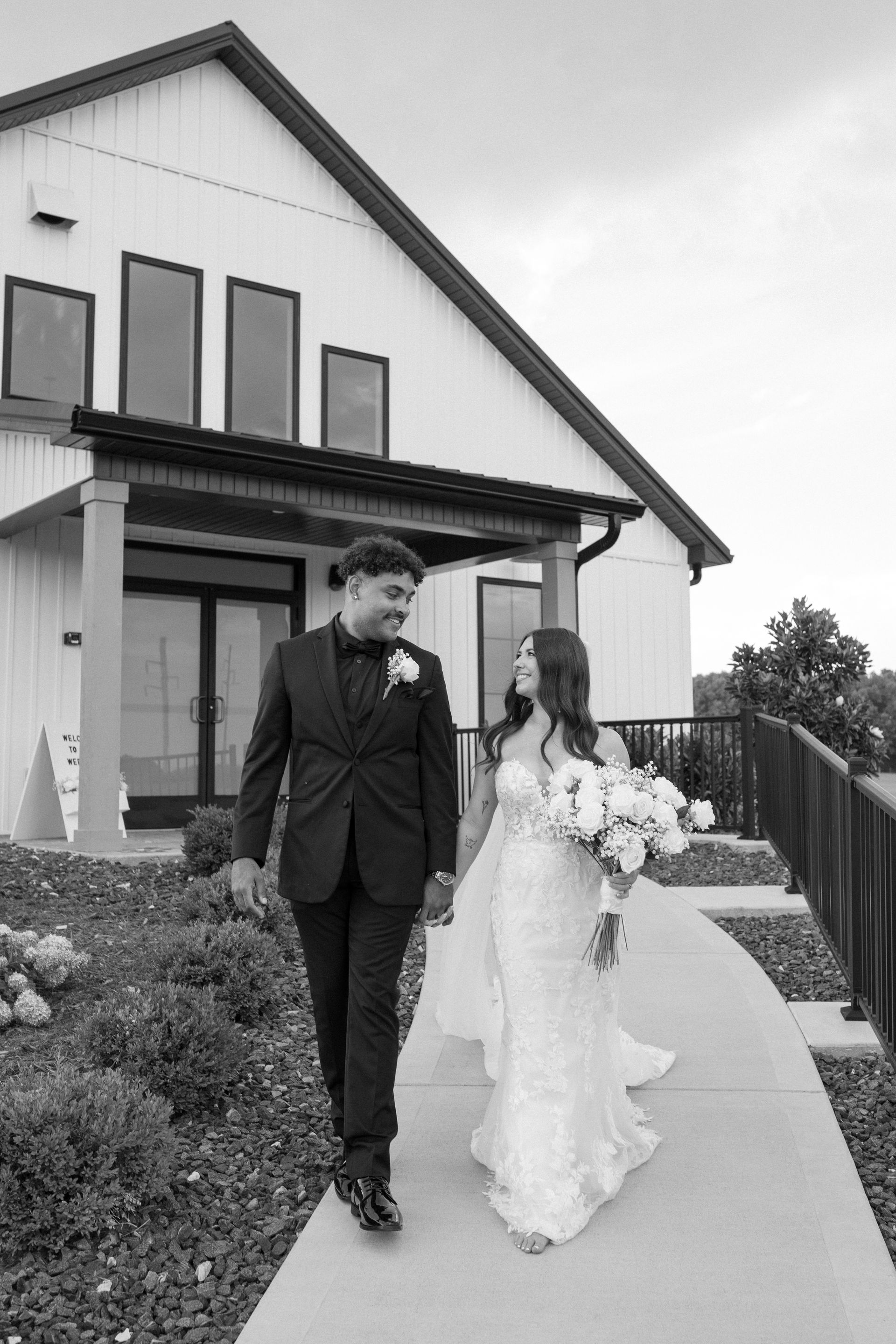A bride and groom are walking down a sidewalk in front of a white building.
