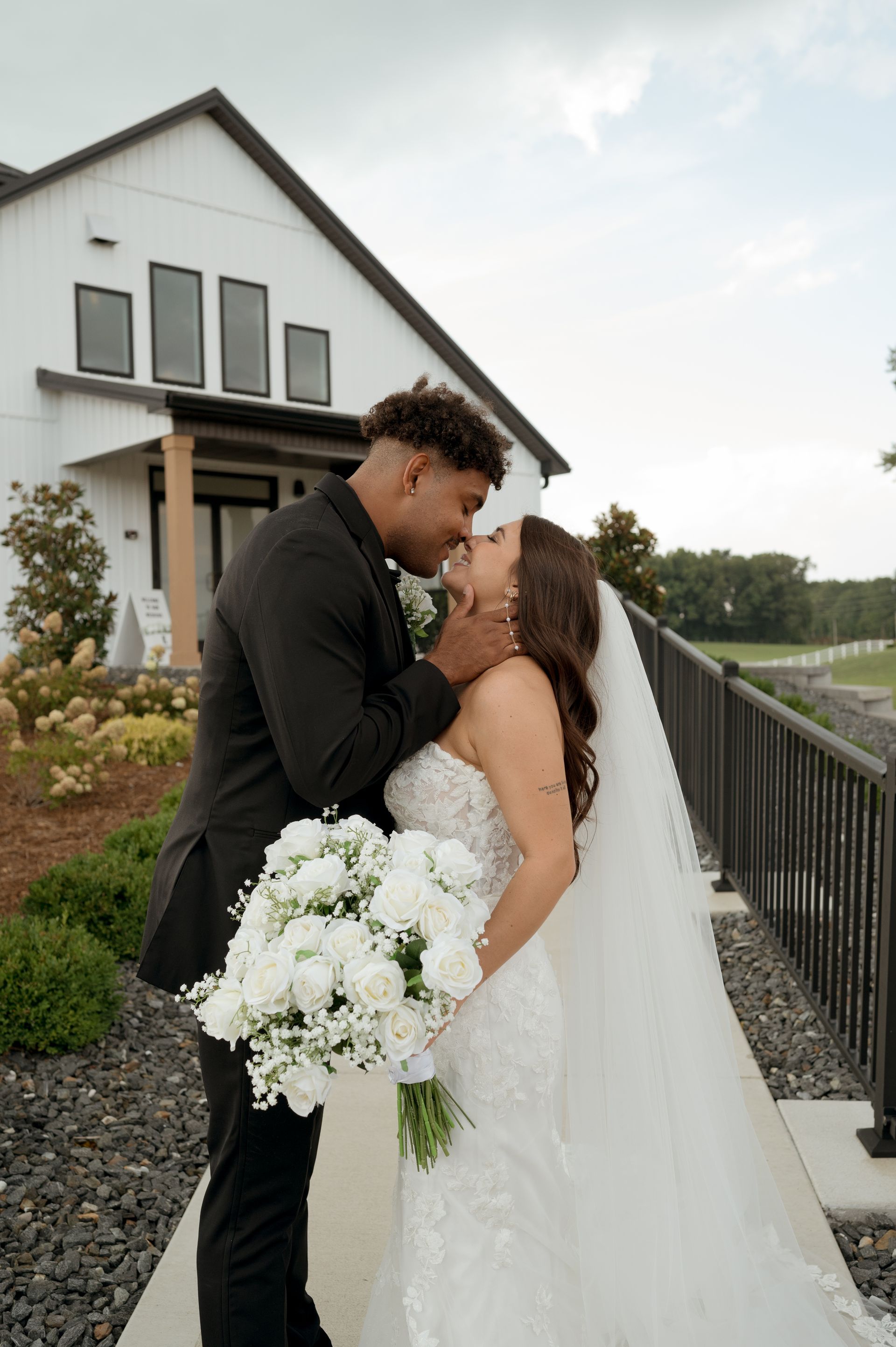 A bride and groom are kissing in front of a white house.