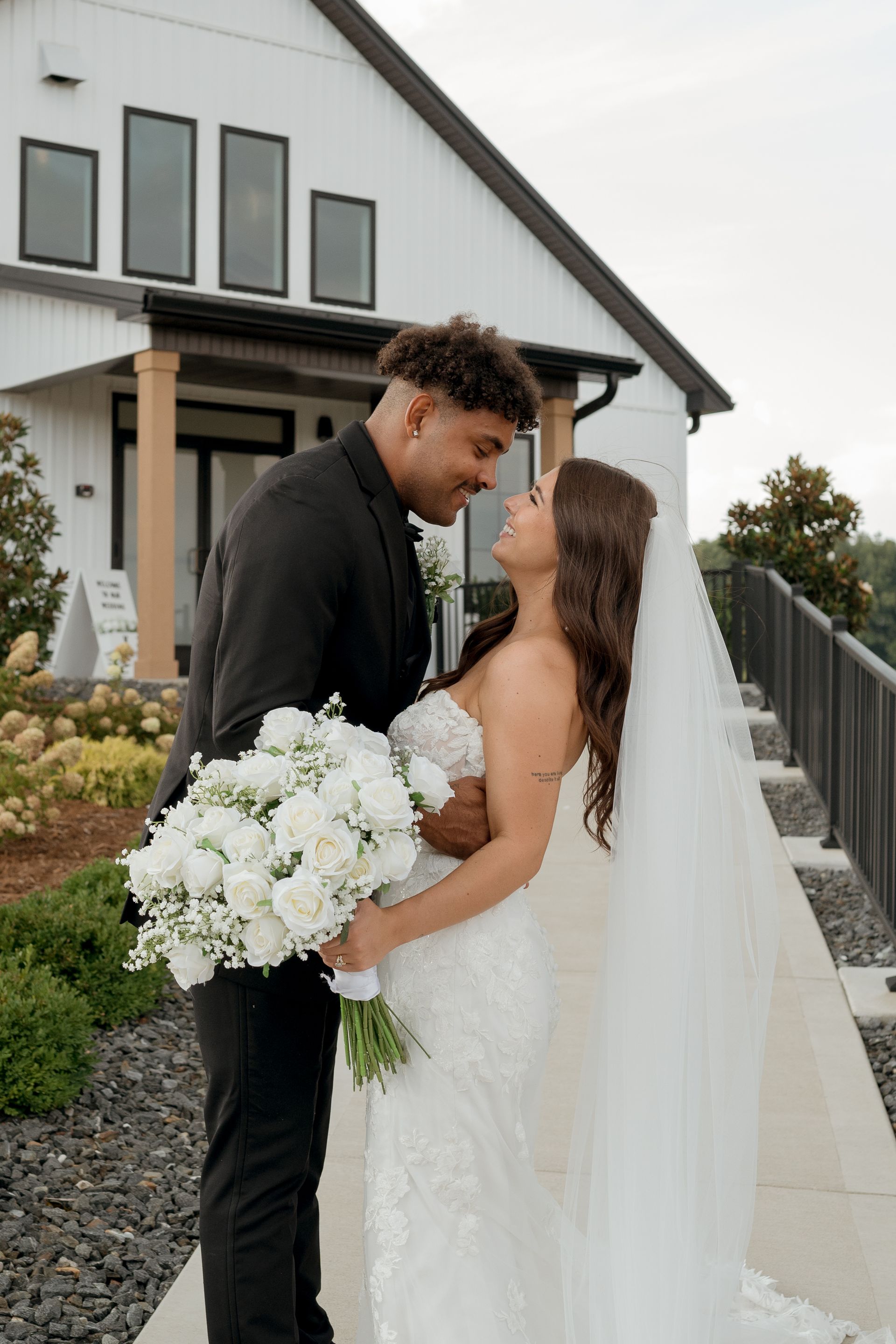 A bride and groom are posing for a picture in front of a white house.