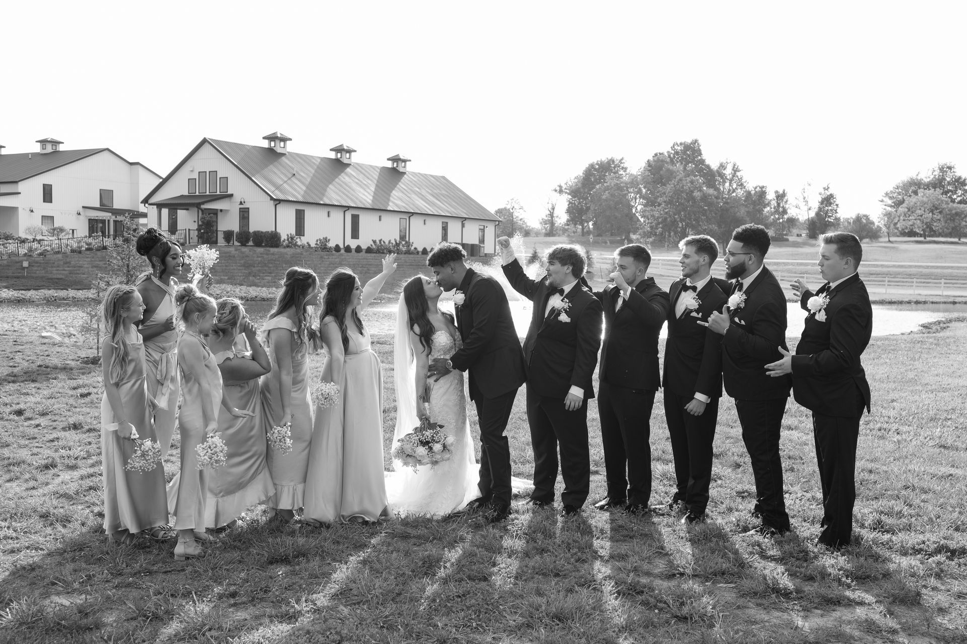 A black and white photo of a bride and groom and their wedding party standing in a field.